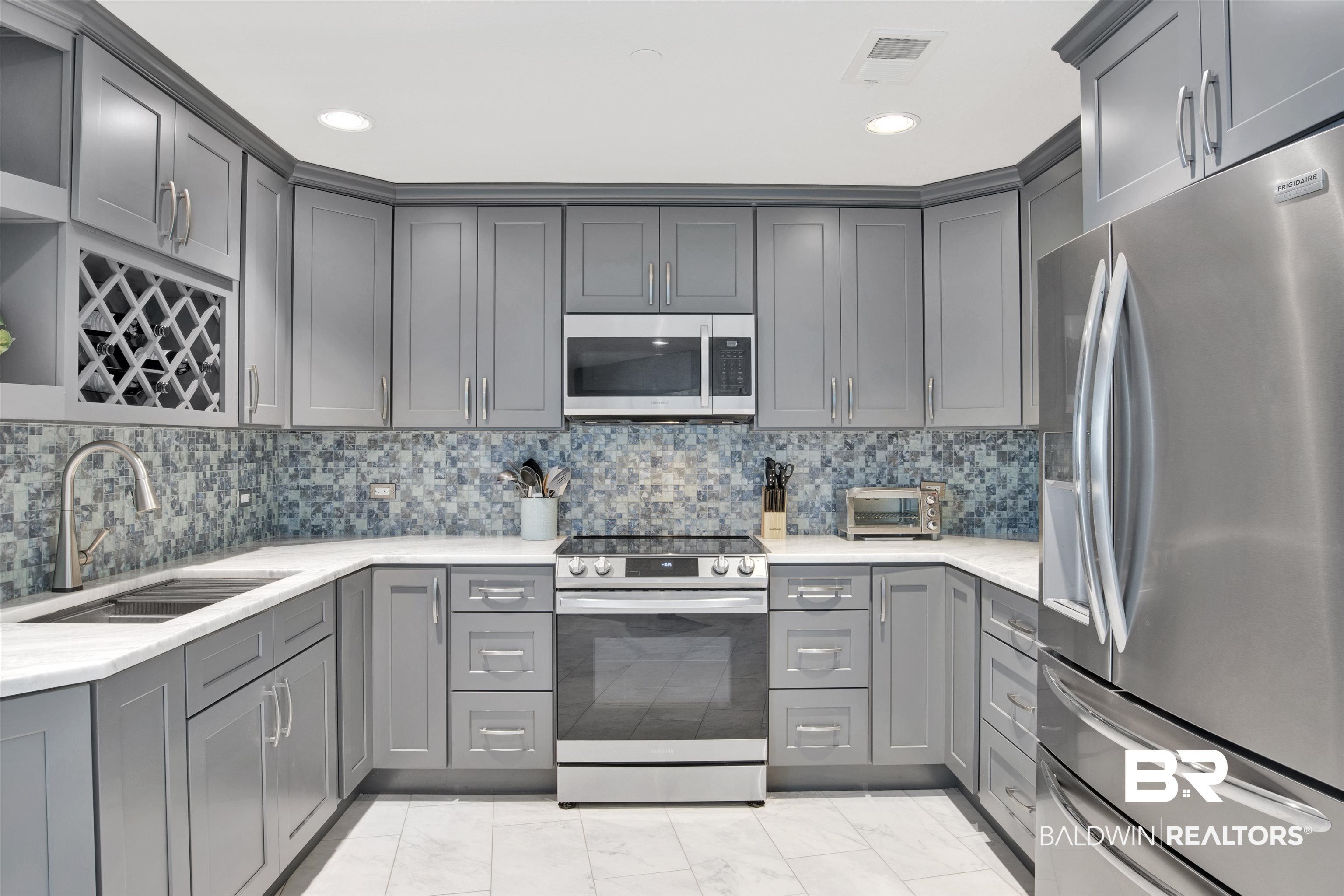 Modern kitchen with gray cabinets, blue mosaic backsplash, stainless steel appliances, and a built-in wine rack.