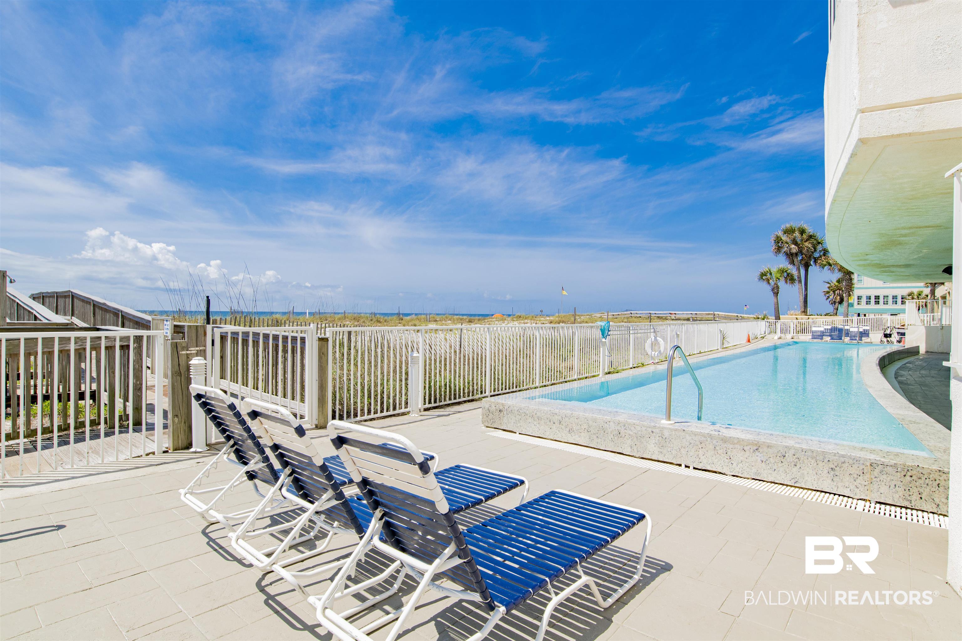 Beachfront condominium pool deck with blue lounge chairs, ocean view, and palm trees.