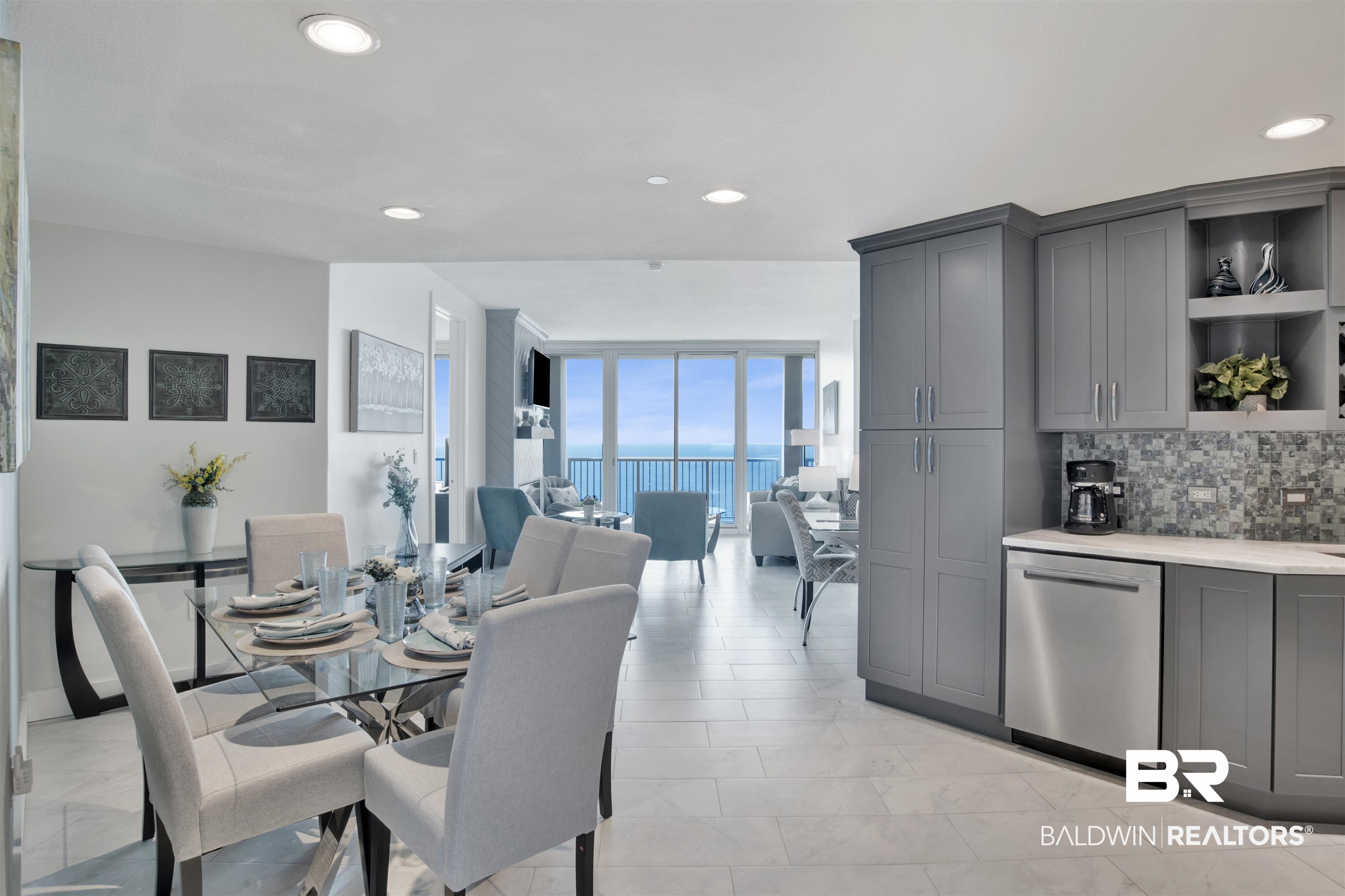 Open-plan condo kitchen and dining area with gray cabinets and a Gulf view through sliding glass doors.