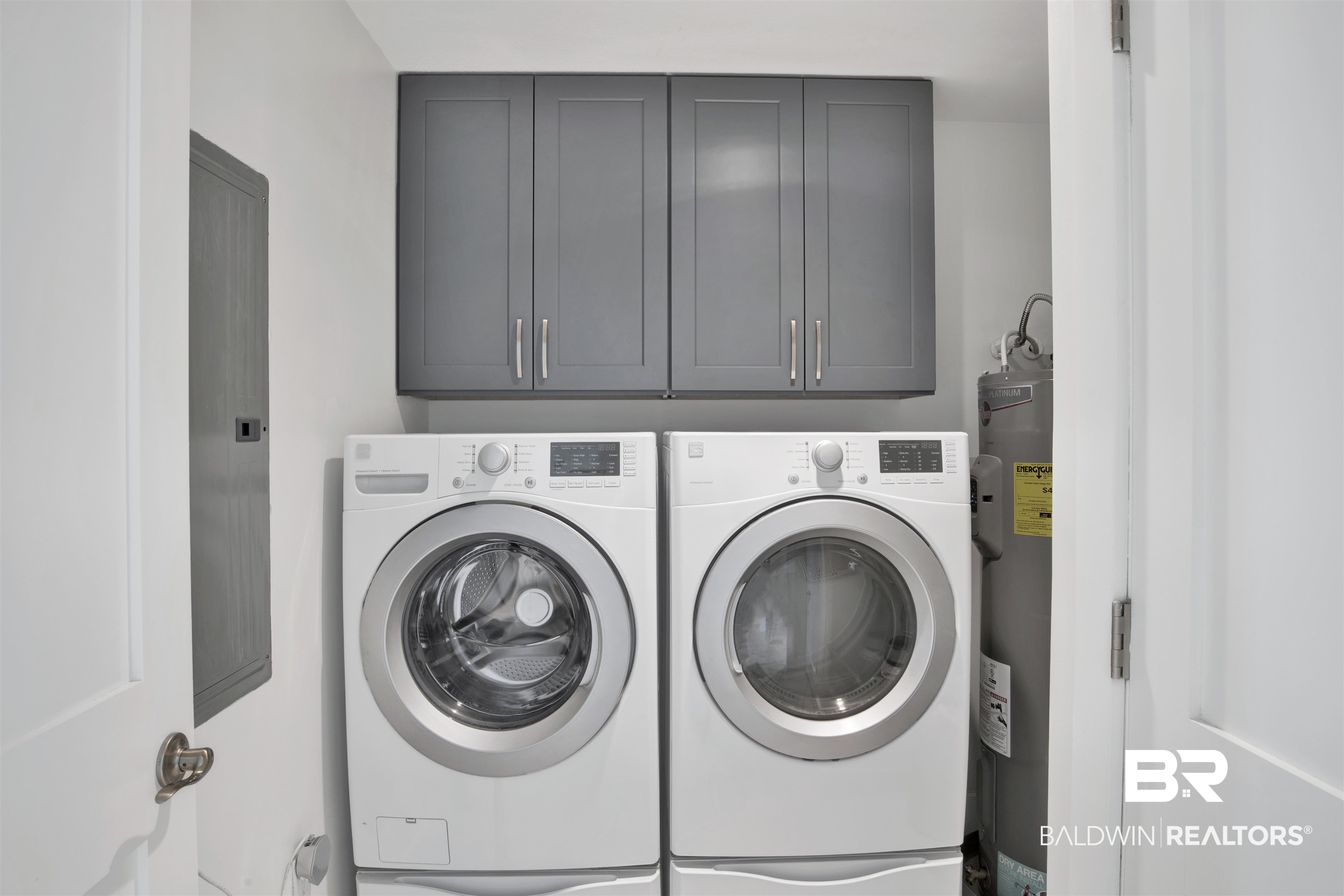 Laundry area with front-loading washer and dryer beneath dark gray cabinets.