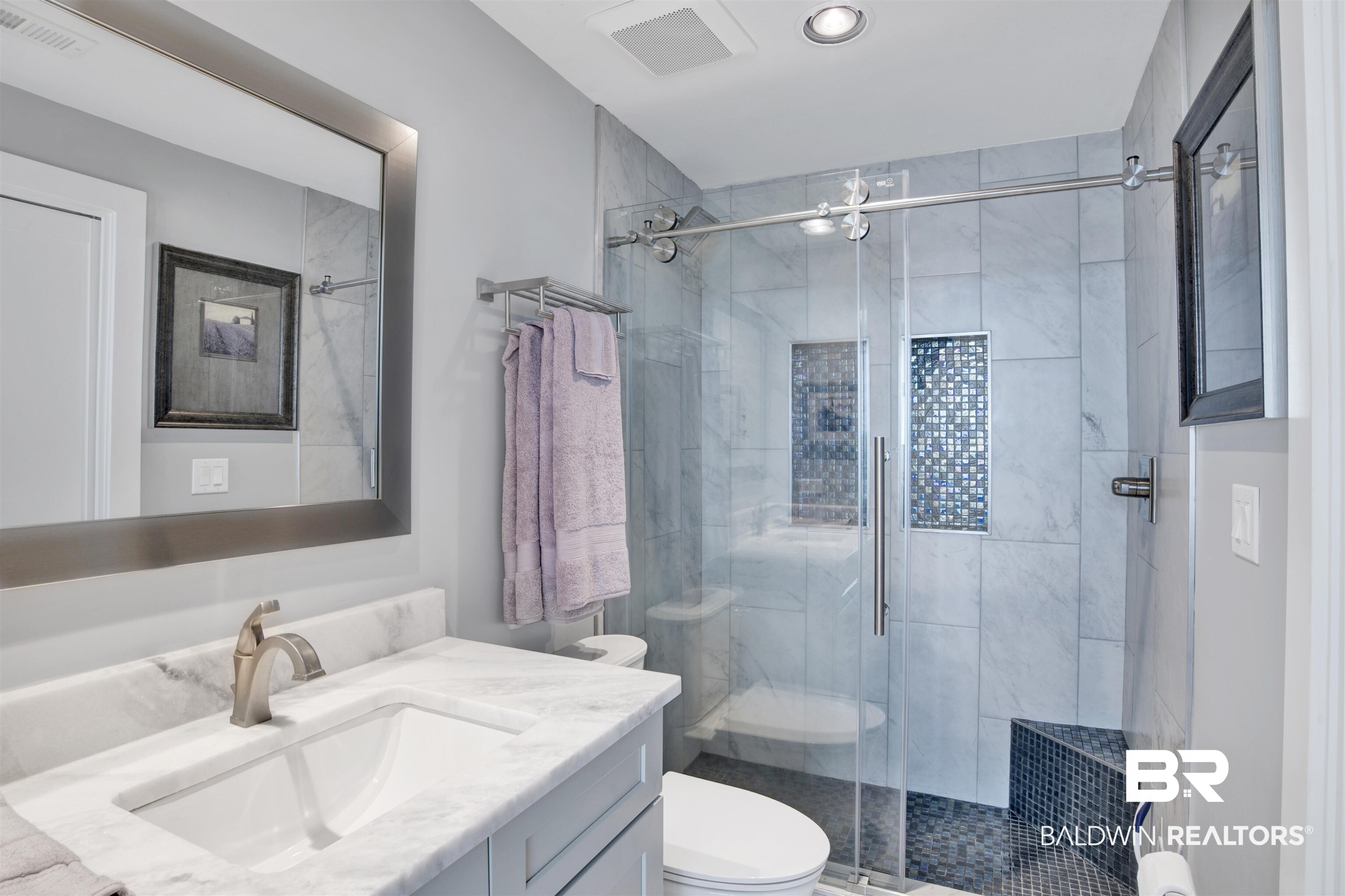 Bathroom with marble vanity and glass shower featuring blue mosaic tile accents.