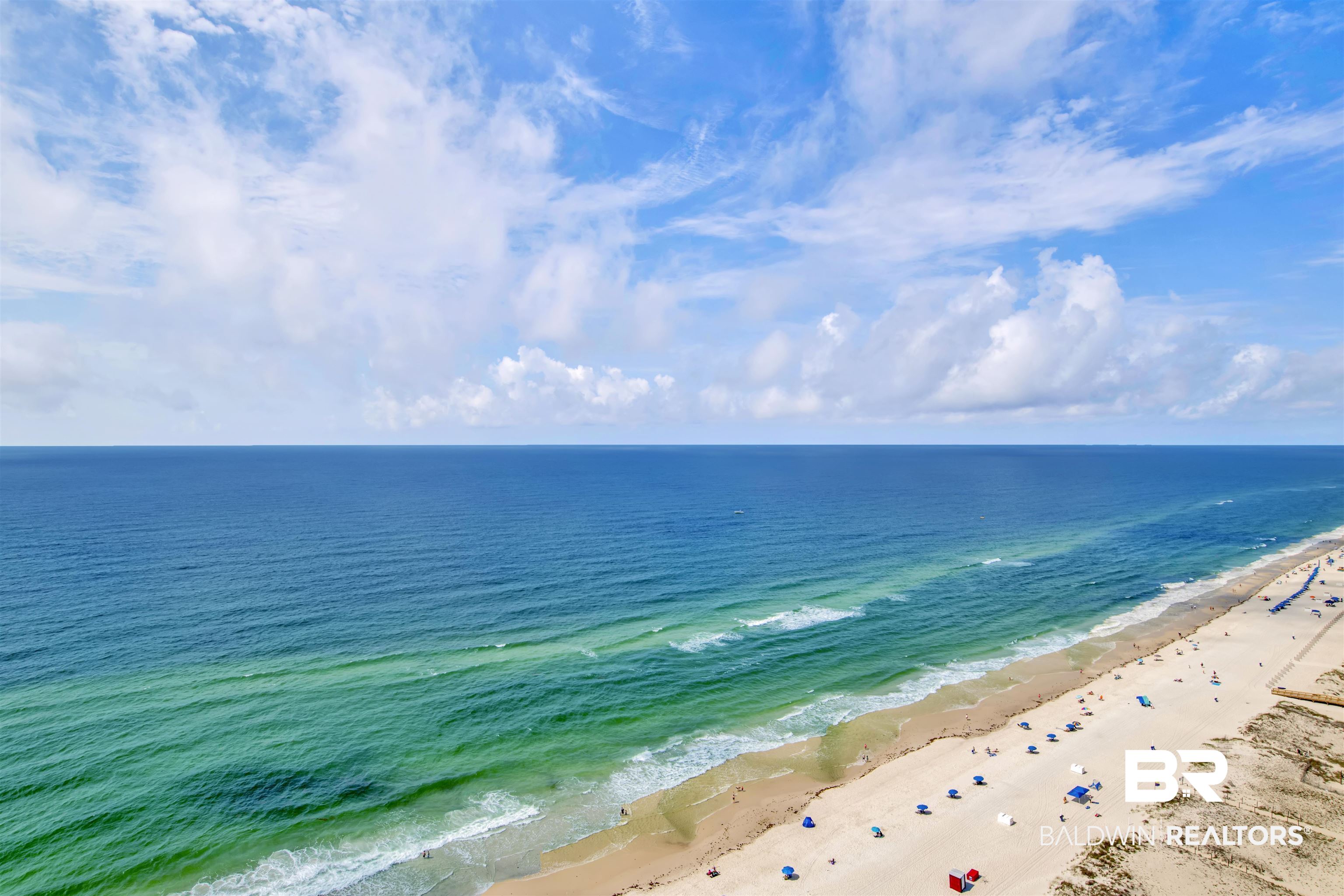 Aerial view of turquoise Gulf water and a sandy beach lined with colorful umbrellas.