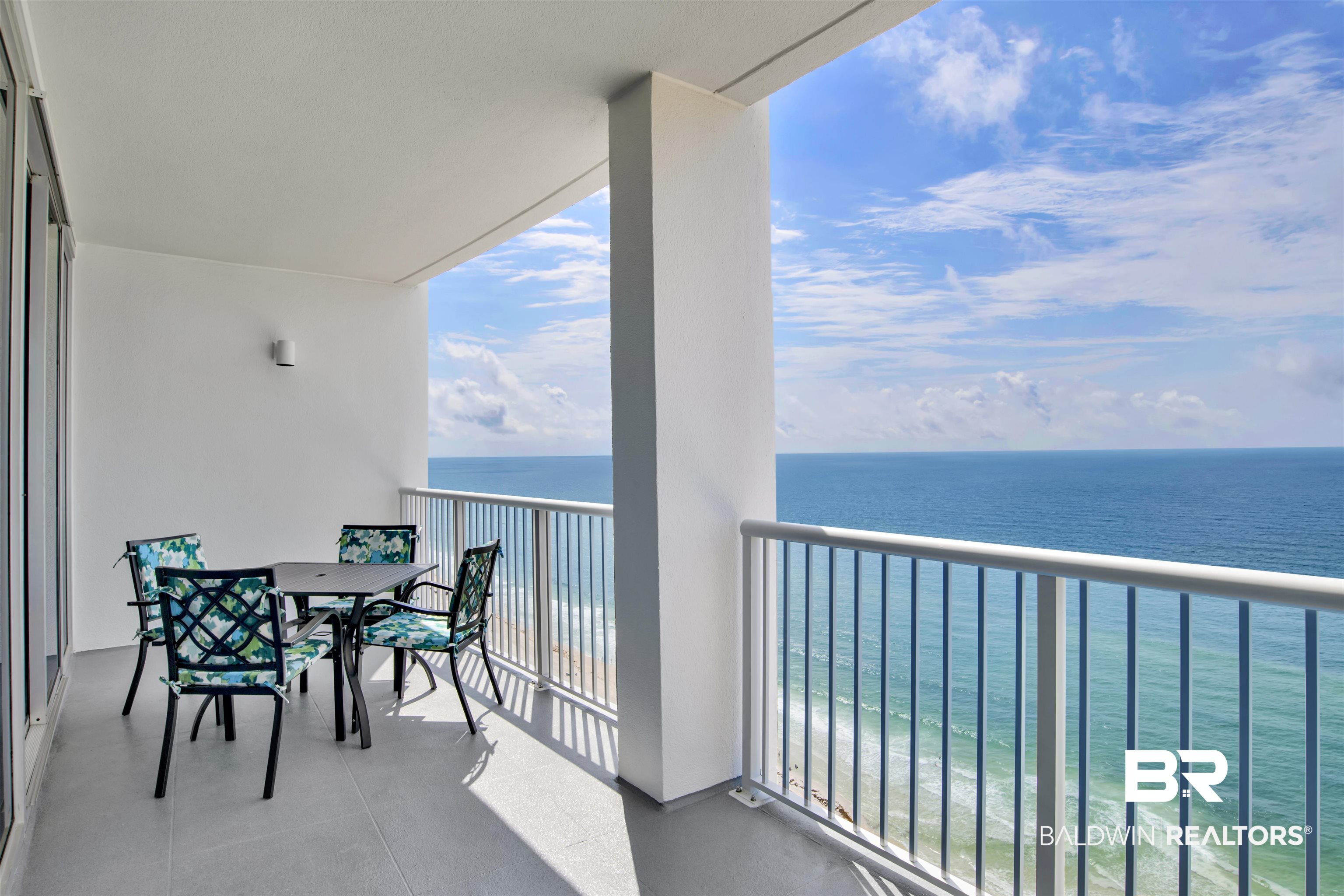 Condo balcony with patterned dining chairs overlooking the Gulf of Mexico.