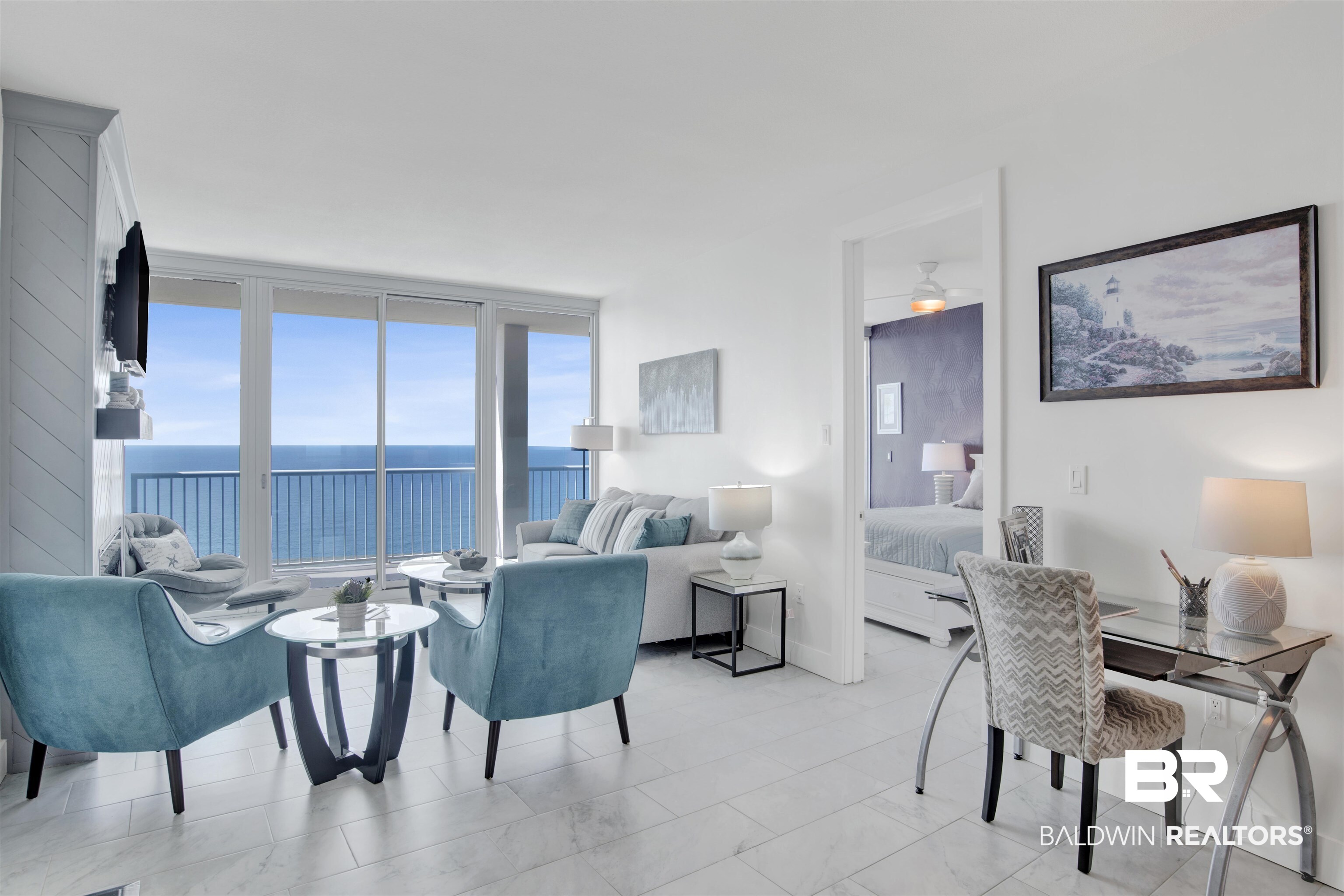 Furnished condo living room with turquoise chairs and sliding doors overlooking the ocean.