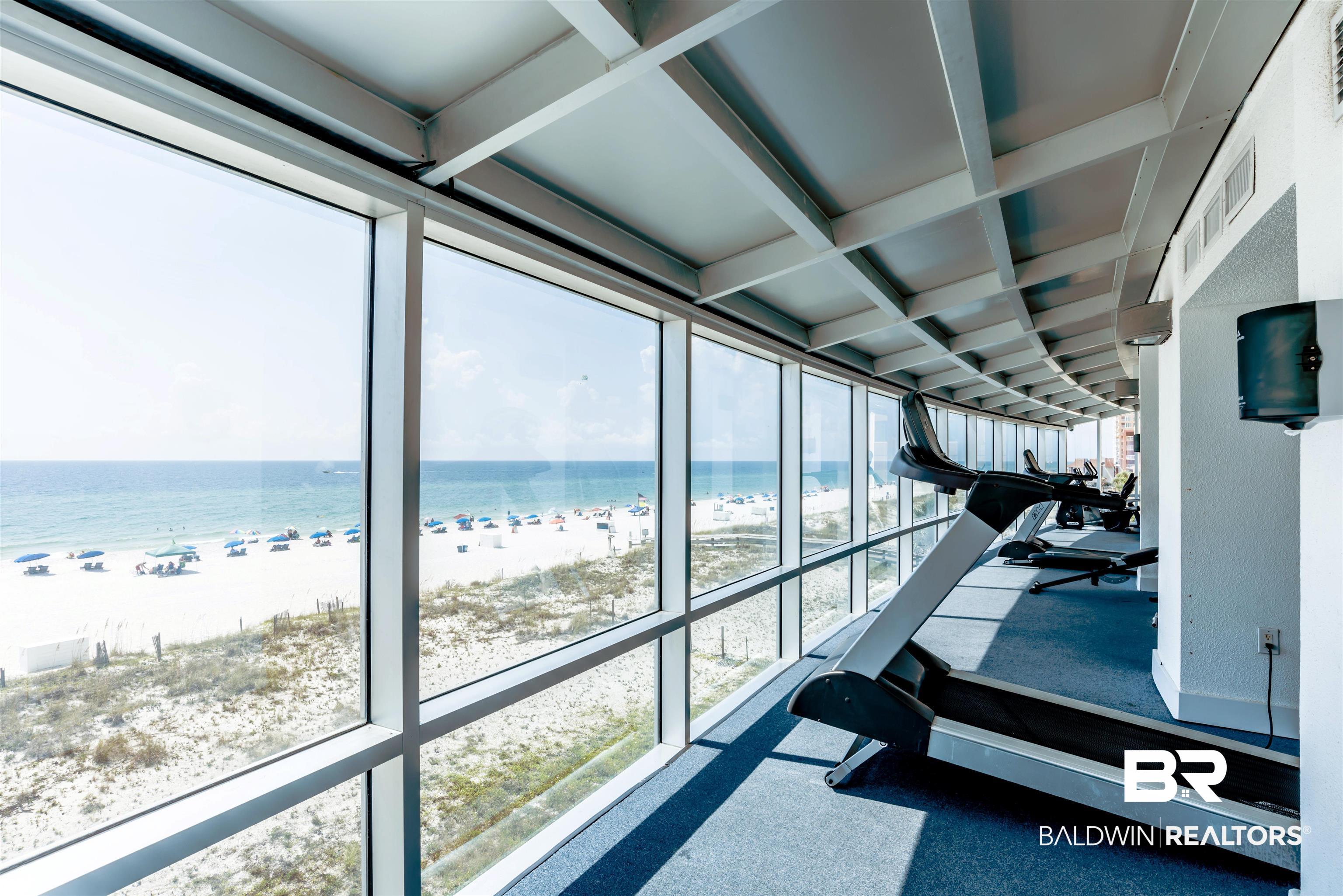 Fitness center with treadmills and floor-to-ceiling windows overlooking the beach and Gulf.
