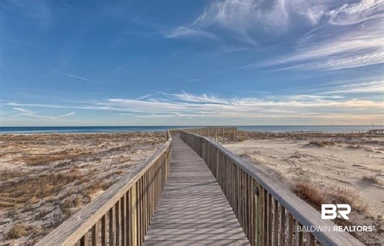 Beach access boardwalk crossing sandy dunes toward the Gulf beneath a blue, cloud-streaked sky.