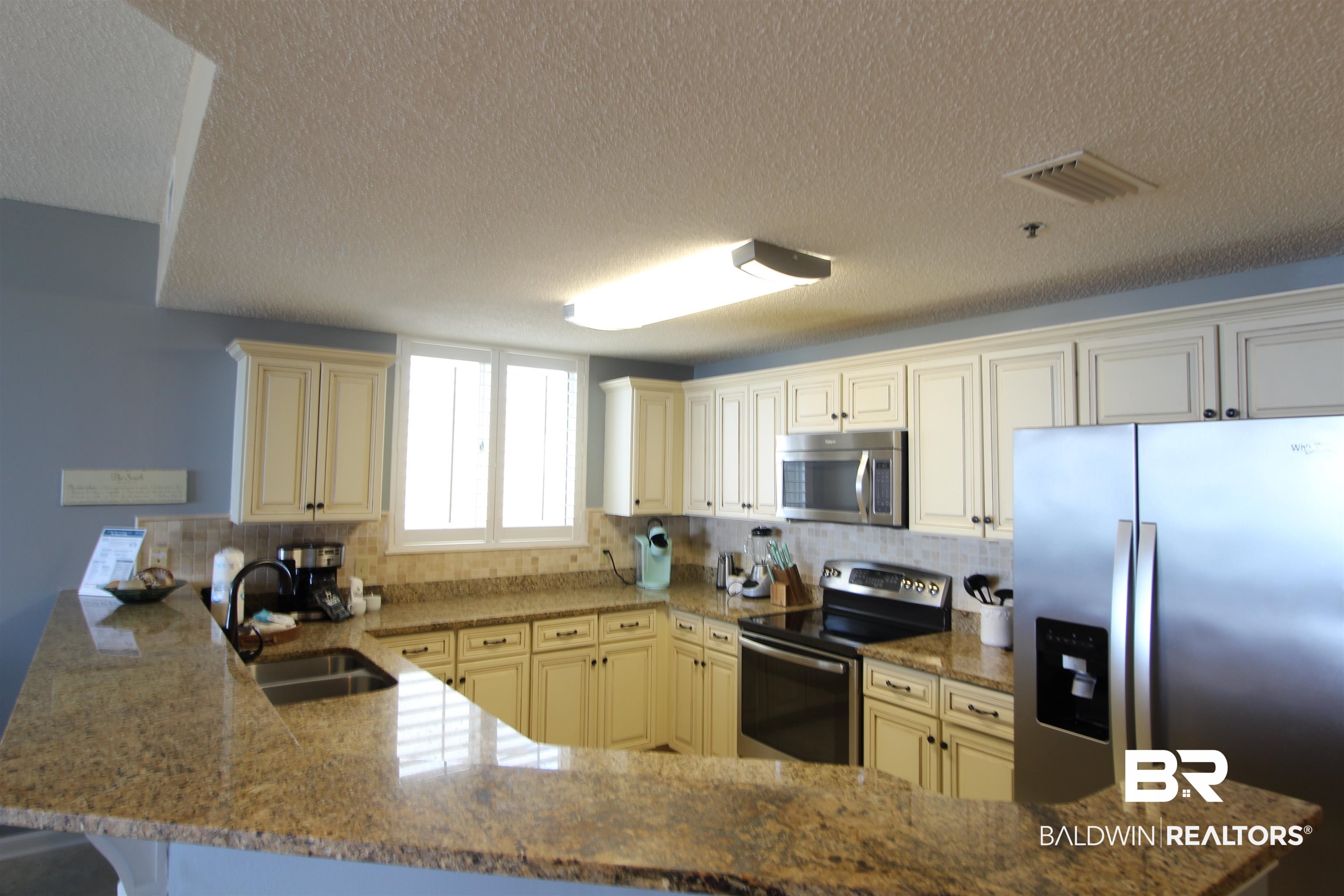 Kitchen with cream cabinets, granite counters, stainless steel appliances, and a sink beneath the window.