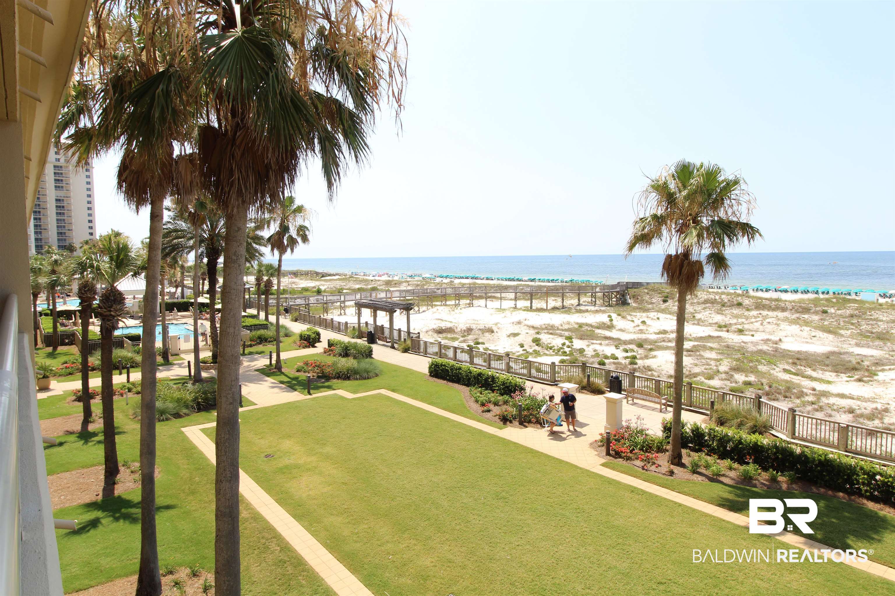Landscaped beachfront grounds with palm trees, a pool, boardwalk, and Gulf shoreline.