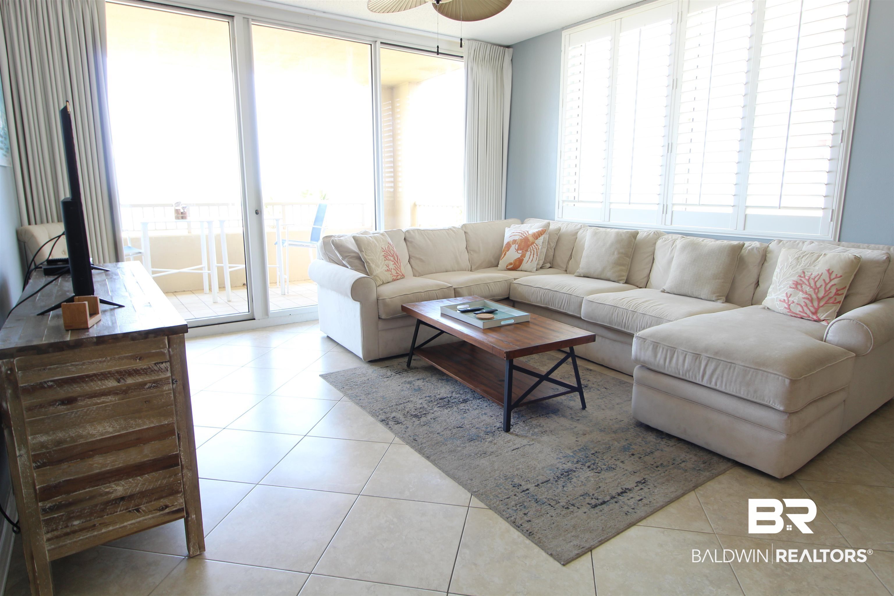 Living room with a cream sectional, coral pillows, and sliding glass doors to a balcony.