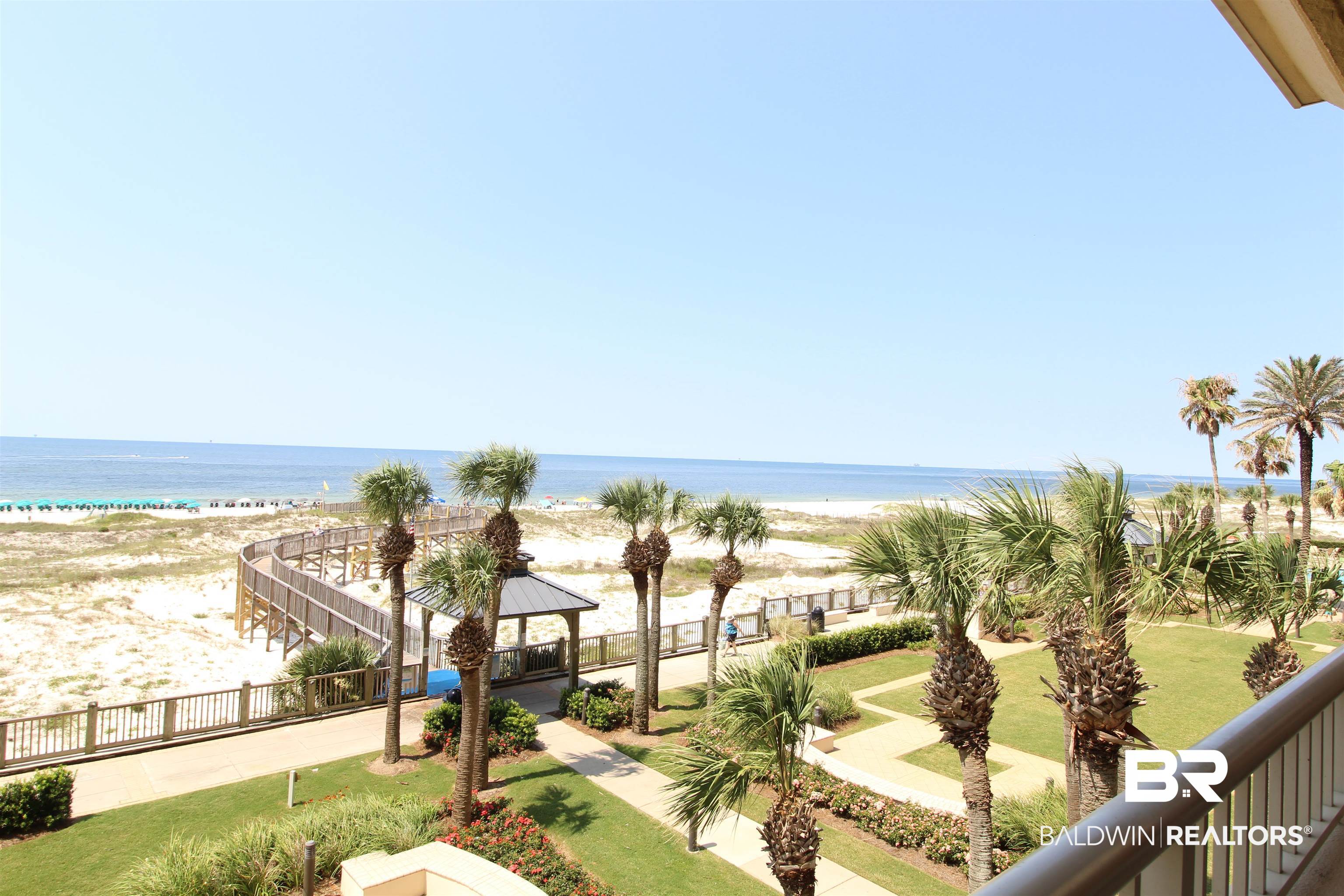 Beachfront view with palm-lined grounds, a boardwalk, sandy dunes, and the Gulf beyond.