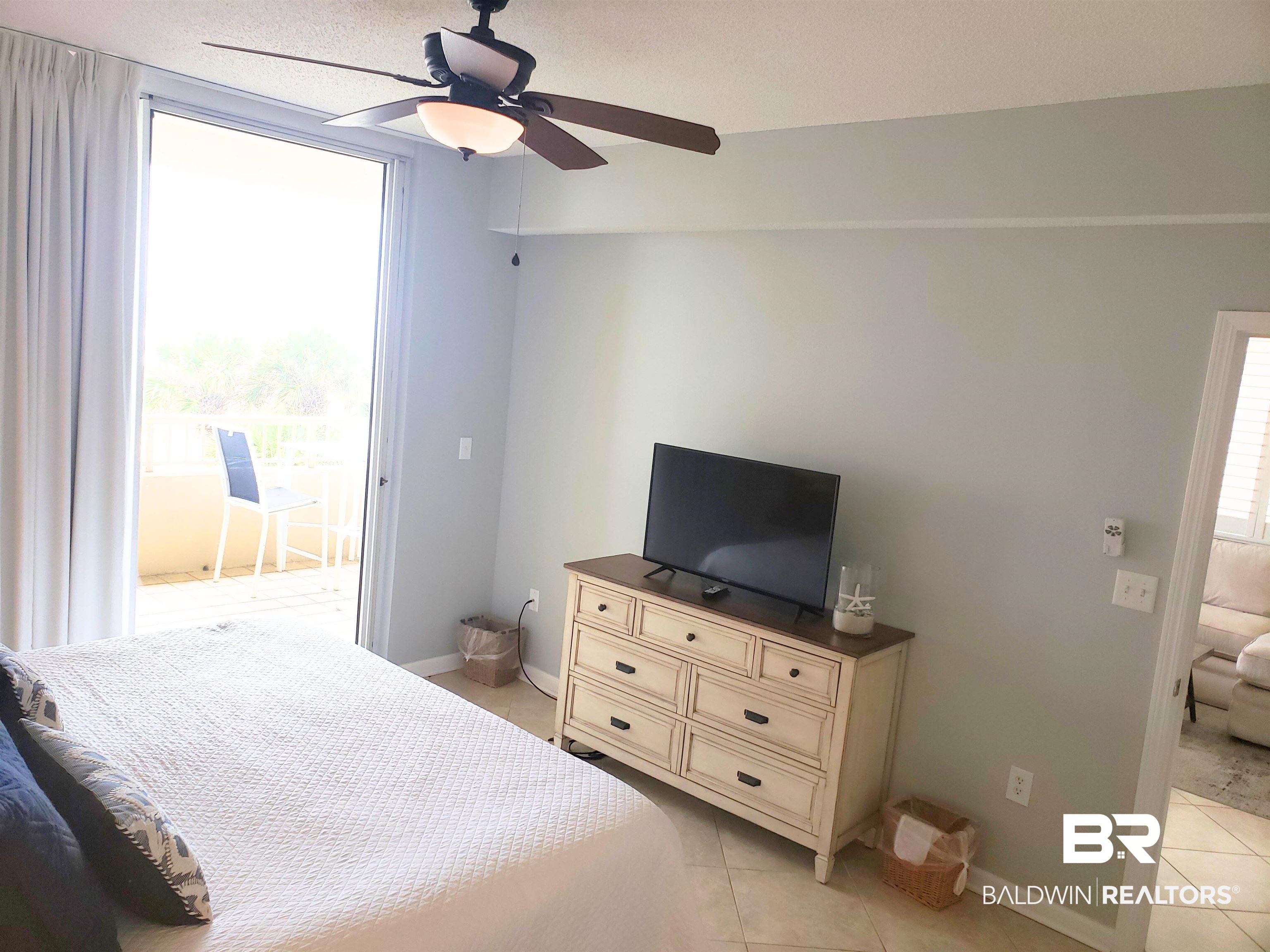 Bedroom with a white quilted bed, television dresser, and sliding door to a balcony.
