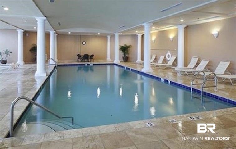 Indoor swimming pool with stone tile decking, white columns, and lounge chairs.