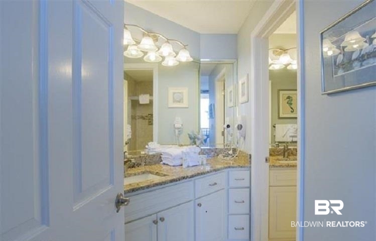Bathroom with pale blue cabinets, granite countertop, large mirrors, and neatly folded white towels.