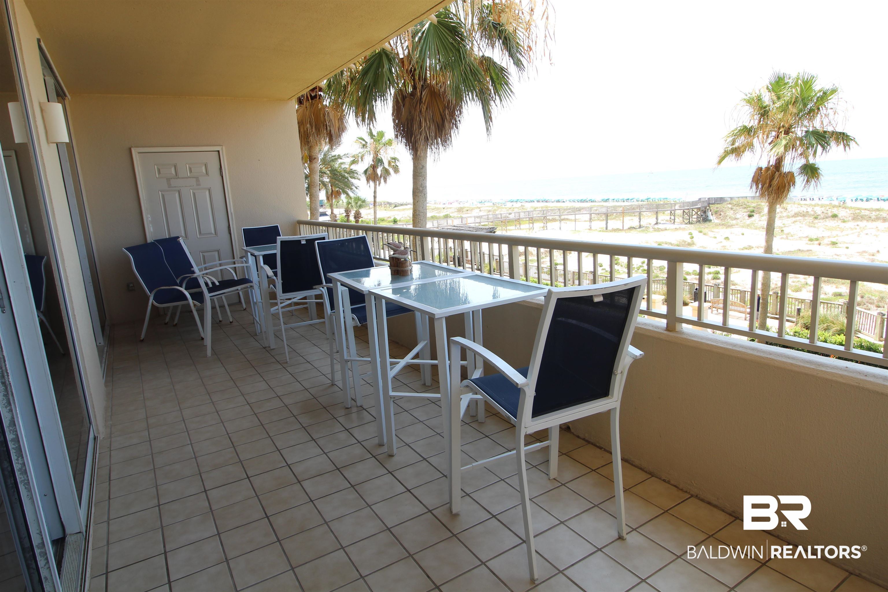 Furnished balcony overlooking palm trees, sandy beach, and Gulf water.