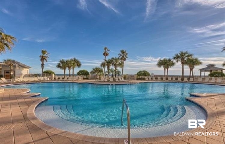Resort pool with a curved shallow entry, central handrail, palm trees, and lounge chairs.