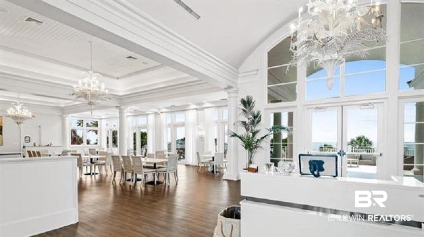 Bright clubhouse lobby with a reception desk, dining tables, chandeliers, and tall windows.