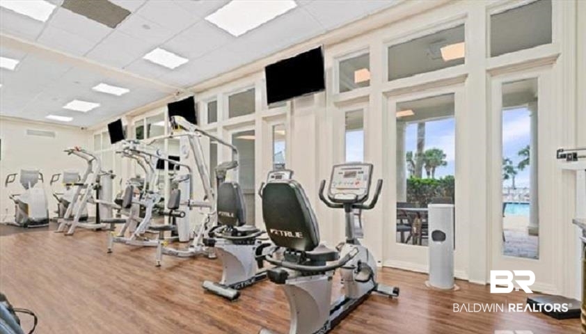 Fitness center with exercise equipment and large windows overlooking a pool and palm trees.