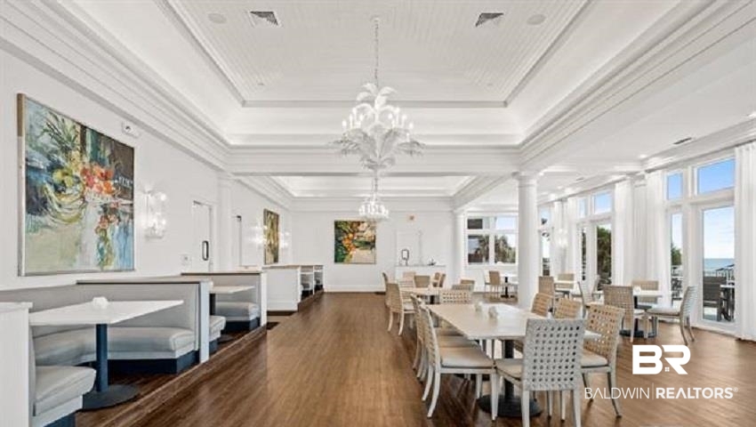 Dining room with white tables, booth seating, chandeliers, and large windows overlooking water.