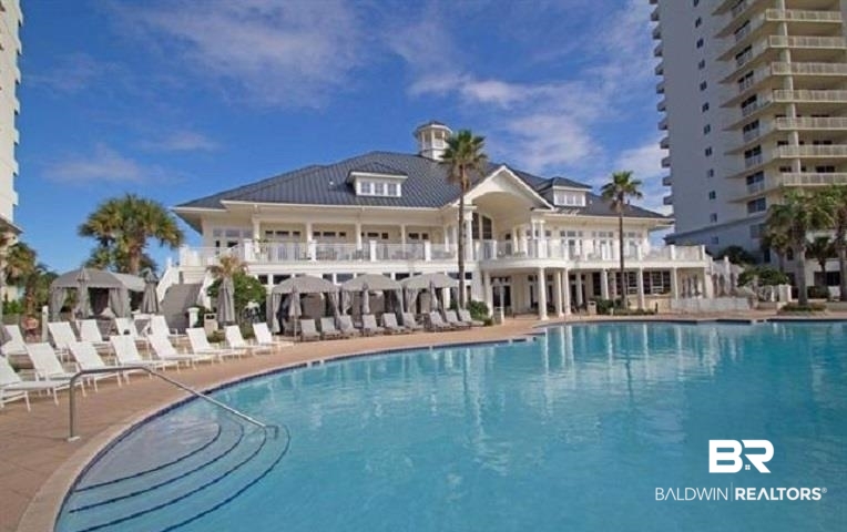 Resort swimming pool with curved entry steps, lounge chairs, cabanas, and a white clubhouse.
