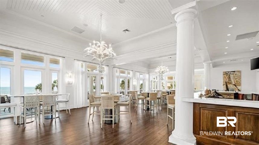 Bright dining room with chandeliers, white columns, and large windows overlooking the water.