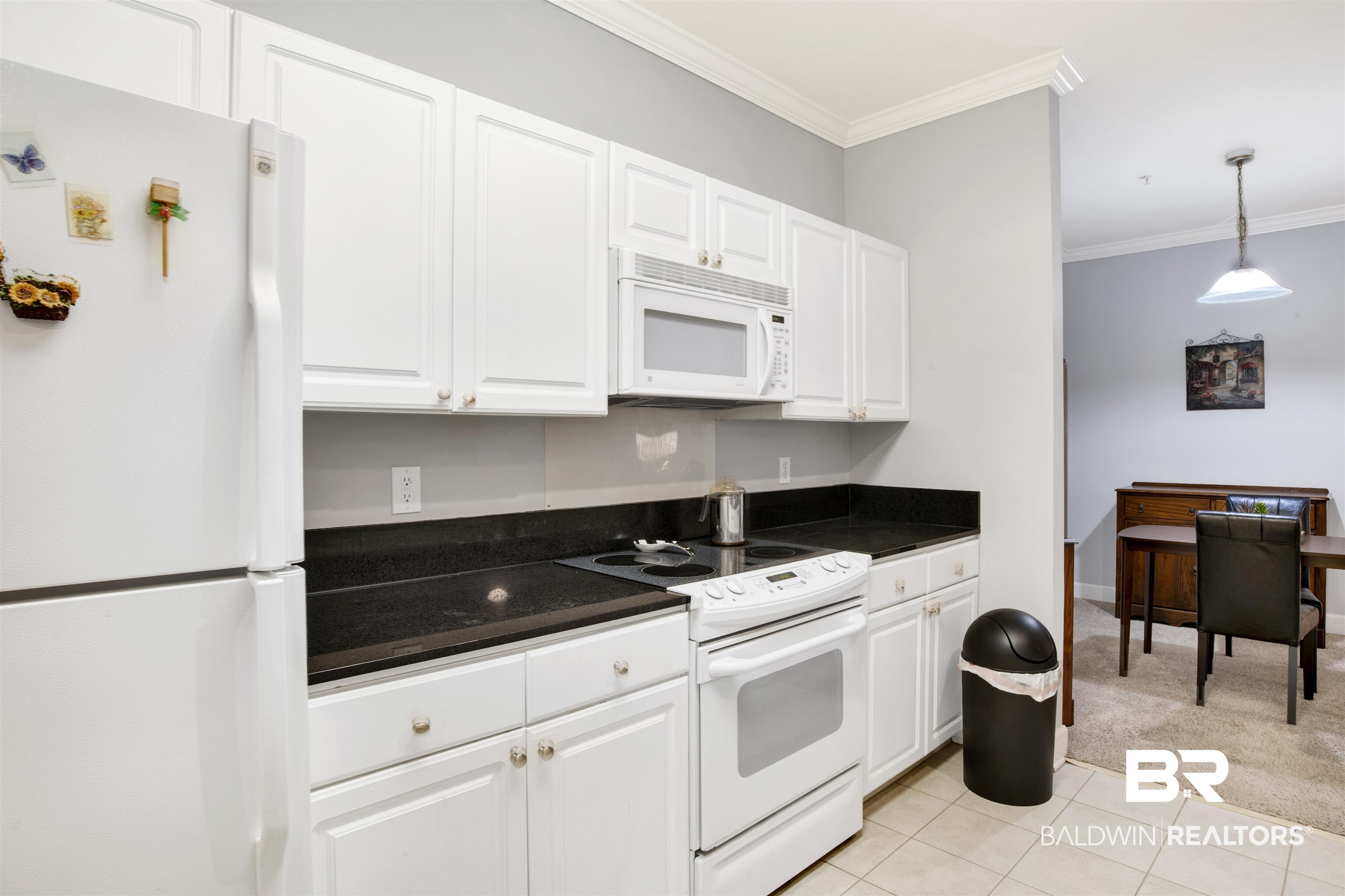 Kitchen with white cabinets, black countertops, and a dining area visible beyond.