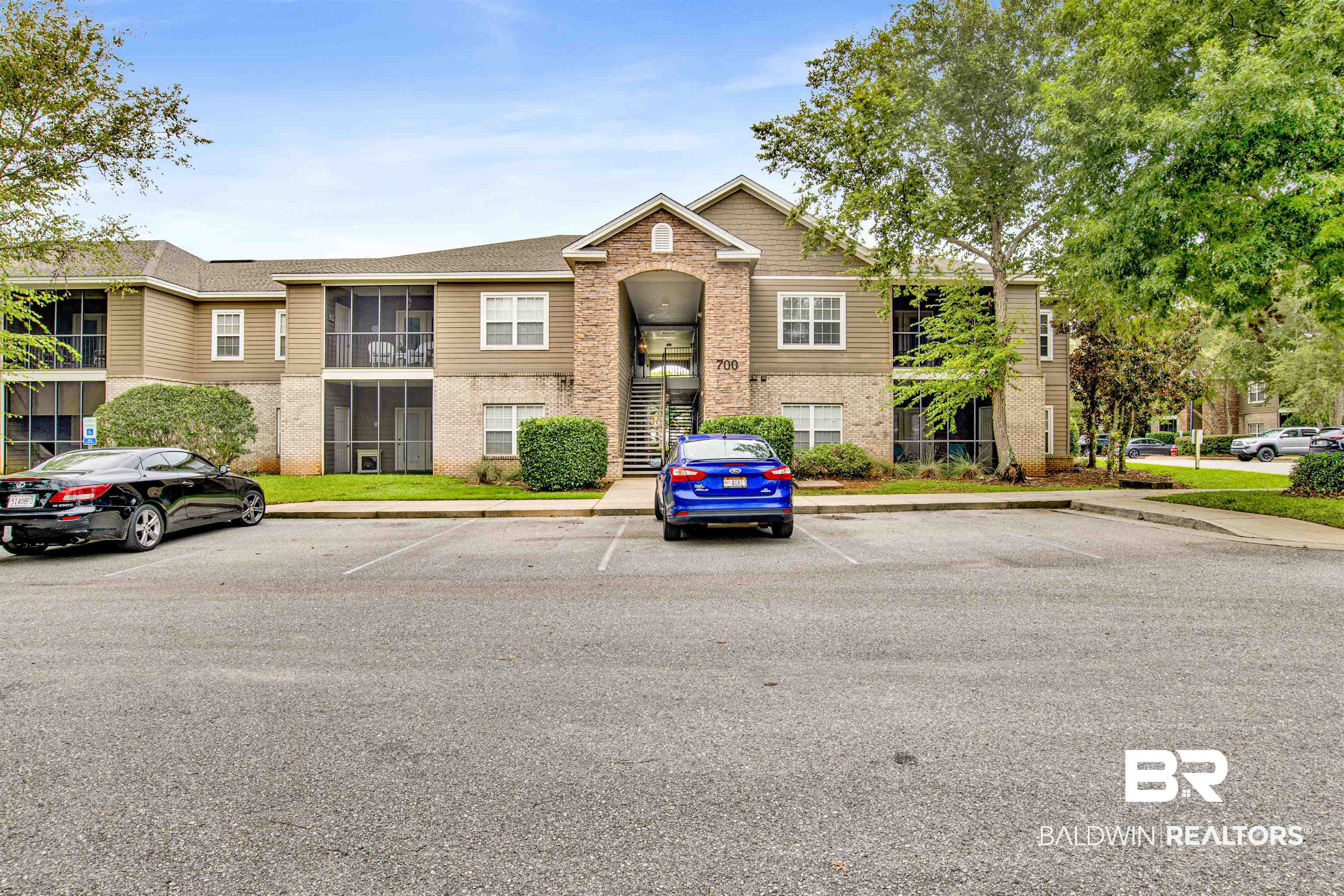 Two-story apartment building with a brick entrance, screened balconies, and parked cars.