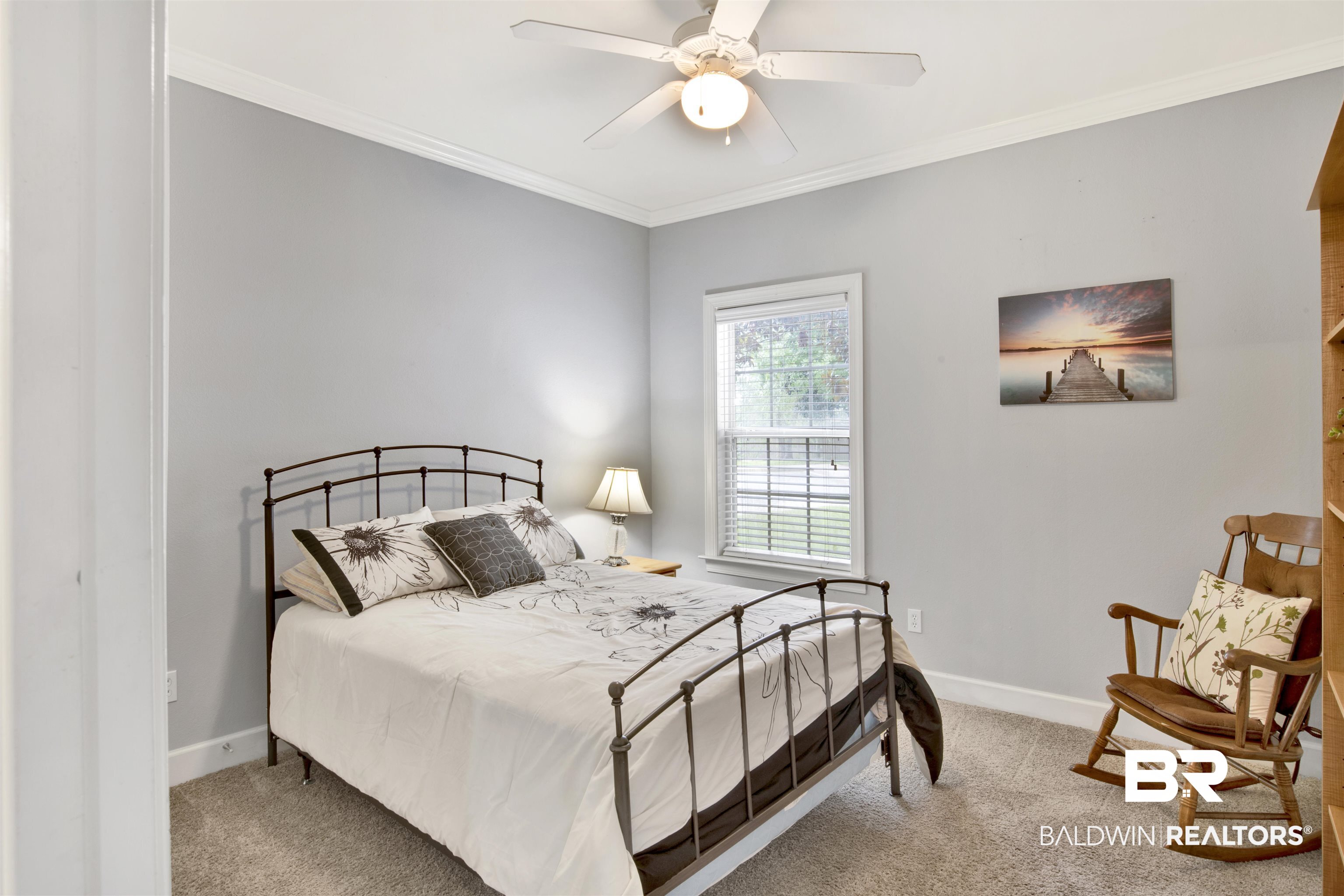 Furnished bedroom with a metal-frame bed, floral bedding, and a wooden rocking chair.