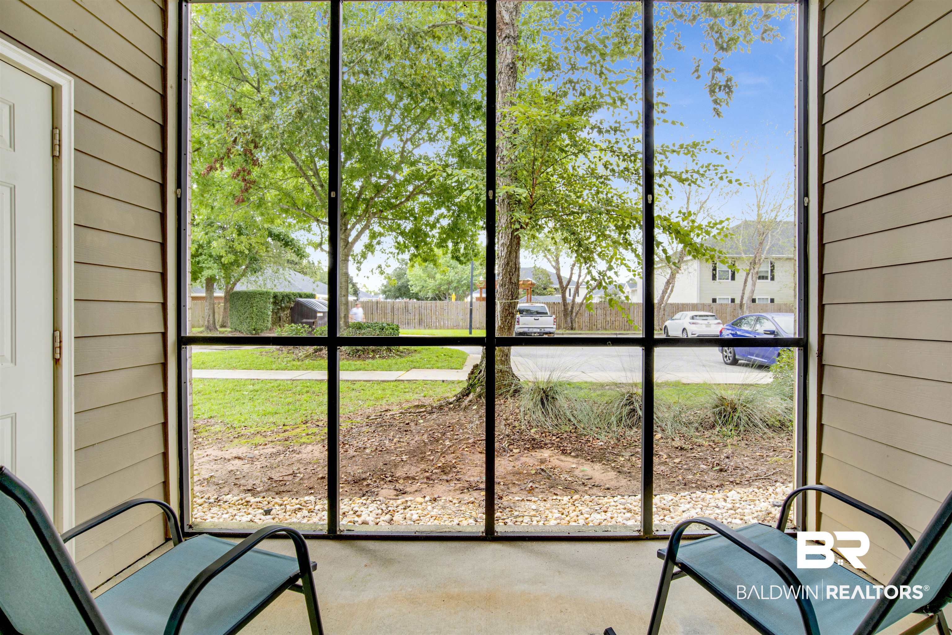 Screened porch with two chairs overlooking leafy trees and a residential street.
