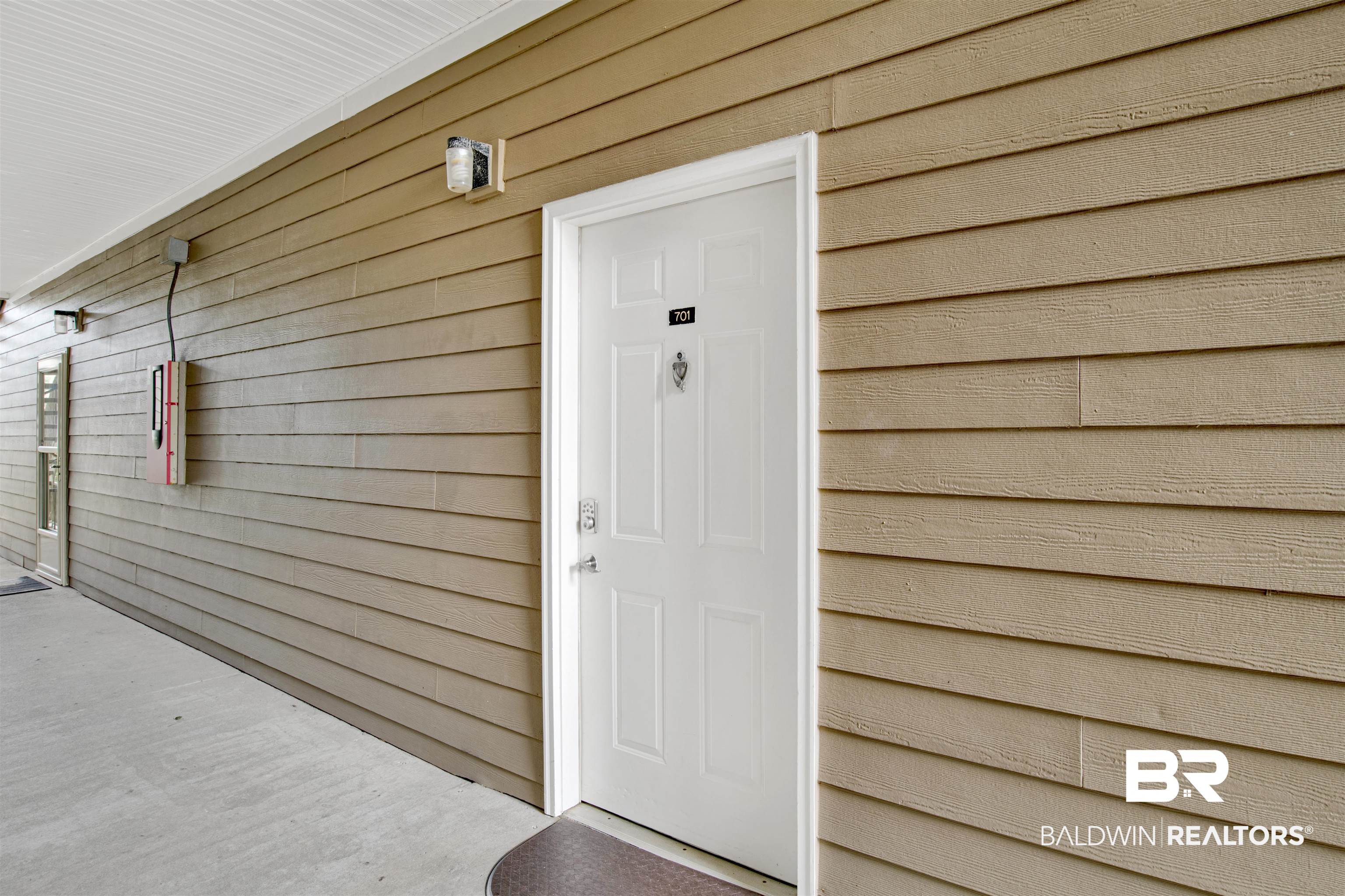 Unit 701’s white paneled entrance door in tan siding, beside a concrete walkway.