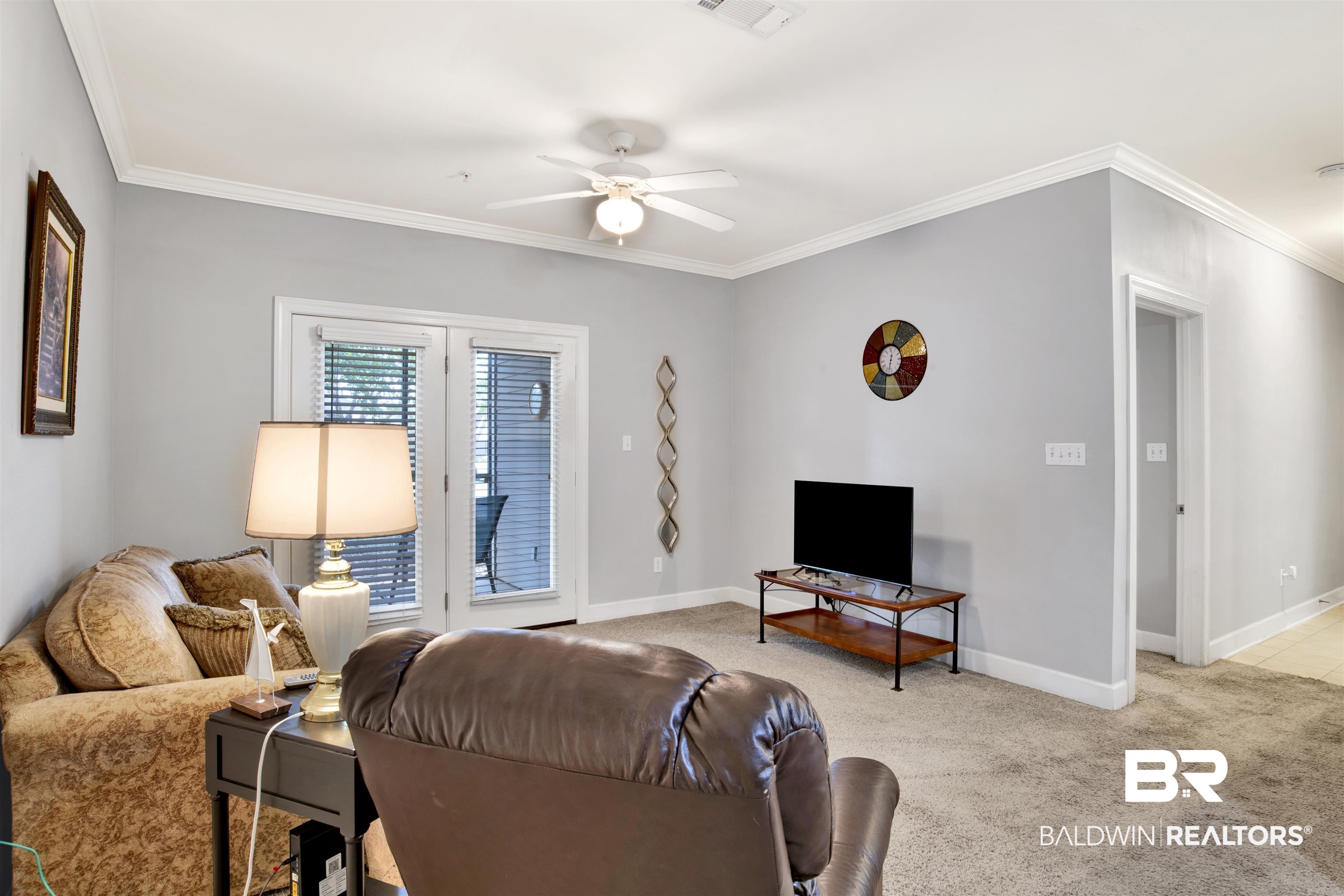 Living room with a patterned sofa, leather recliner, and television beside glass doors with blinds.