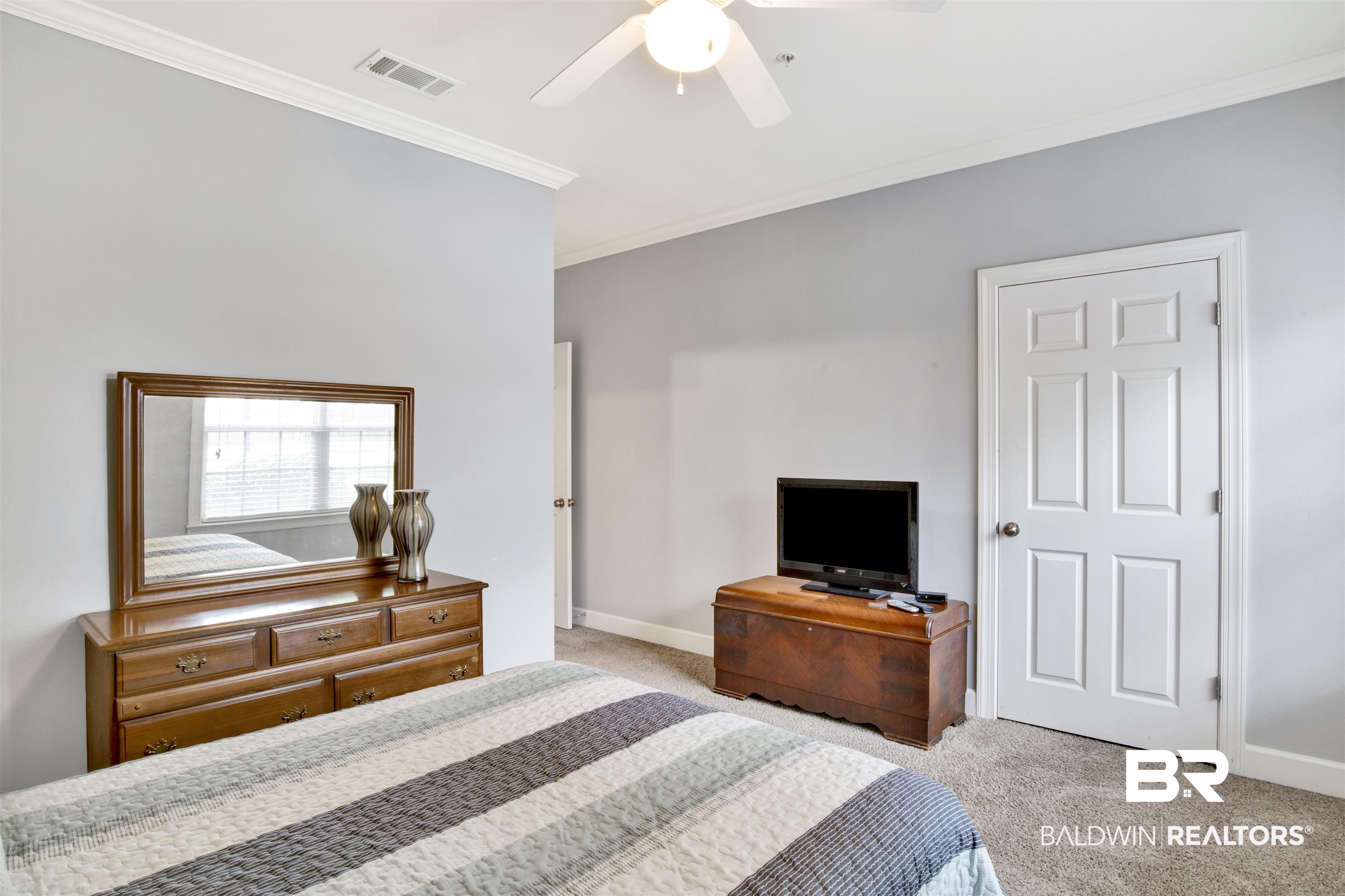 Bedroom with a striped bedspread, wooden dresser and mirror, and television on a chest.