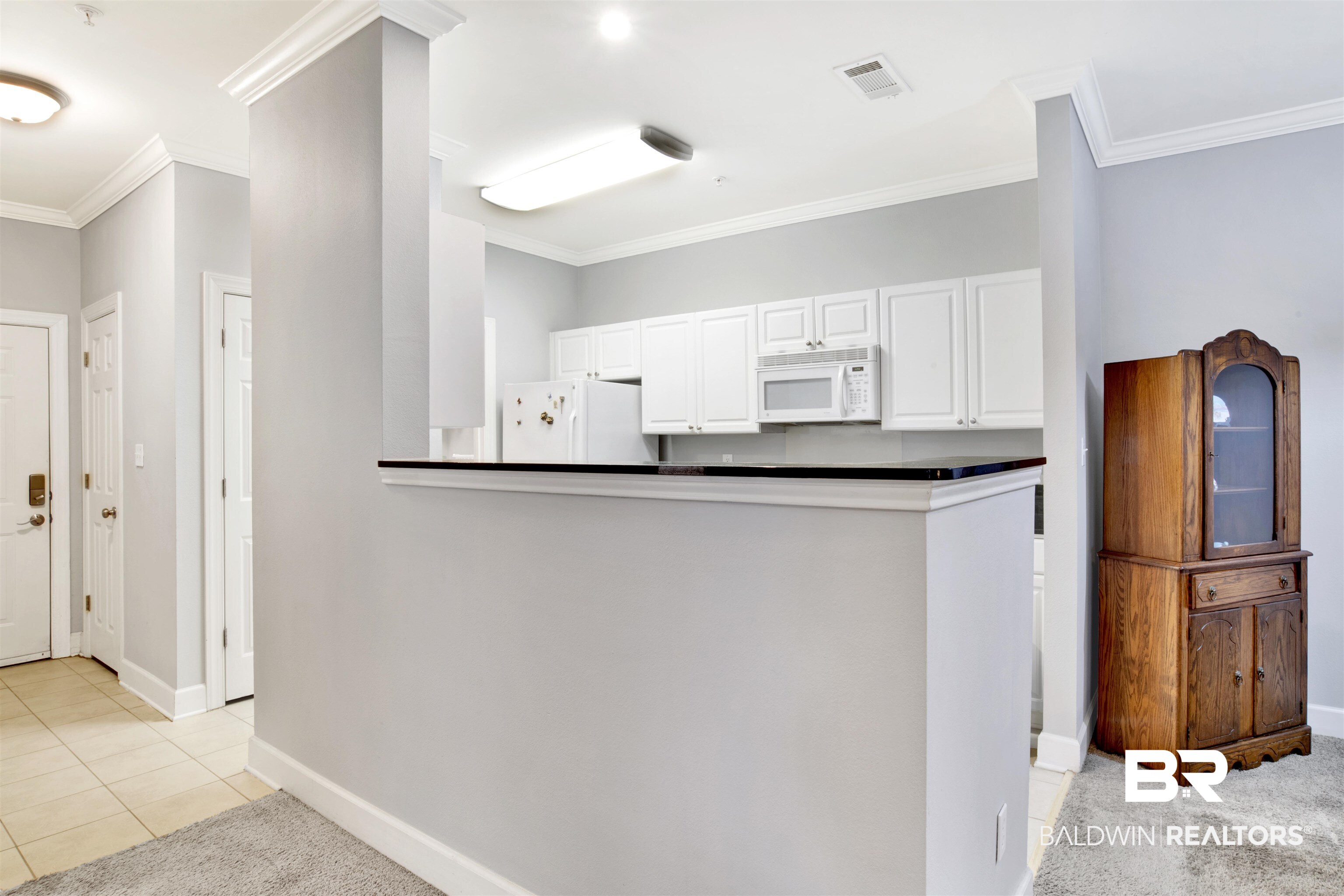 Kitchen with white cabinets, a dark-counter peninsula, and a wooden glass-front cabinet.