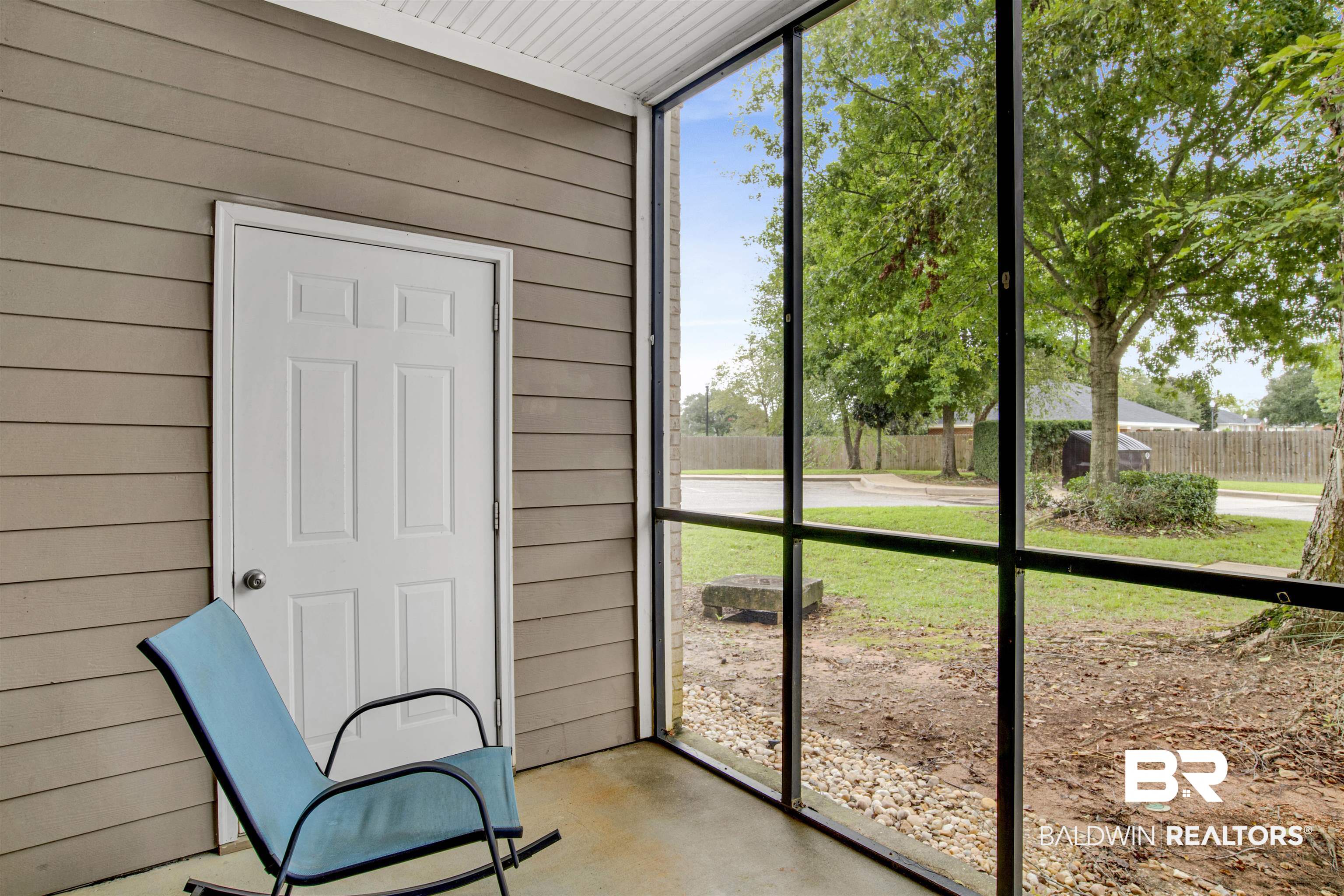 Screened porch with a blue rocking chair overlooking a leafy yard.