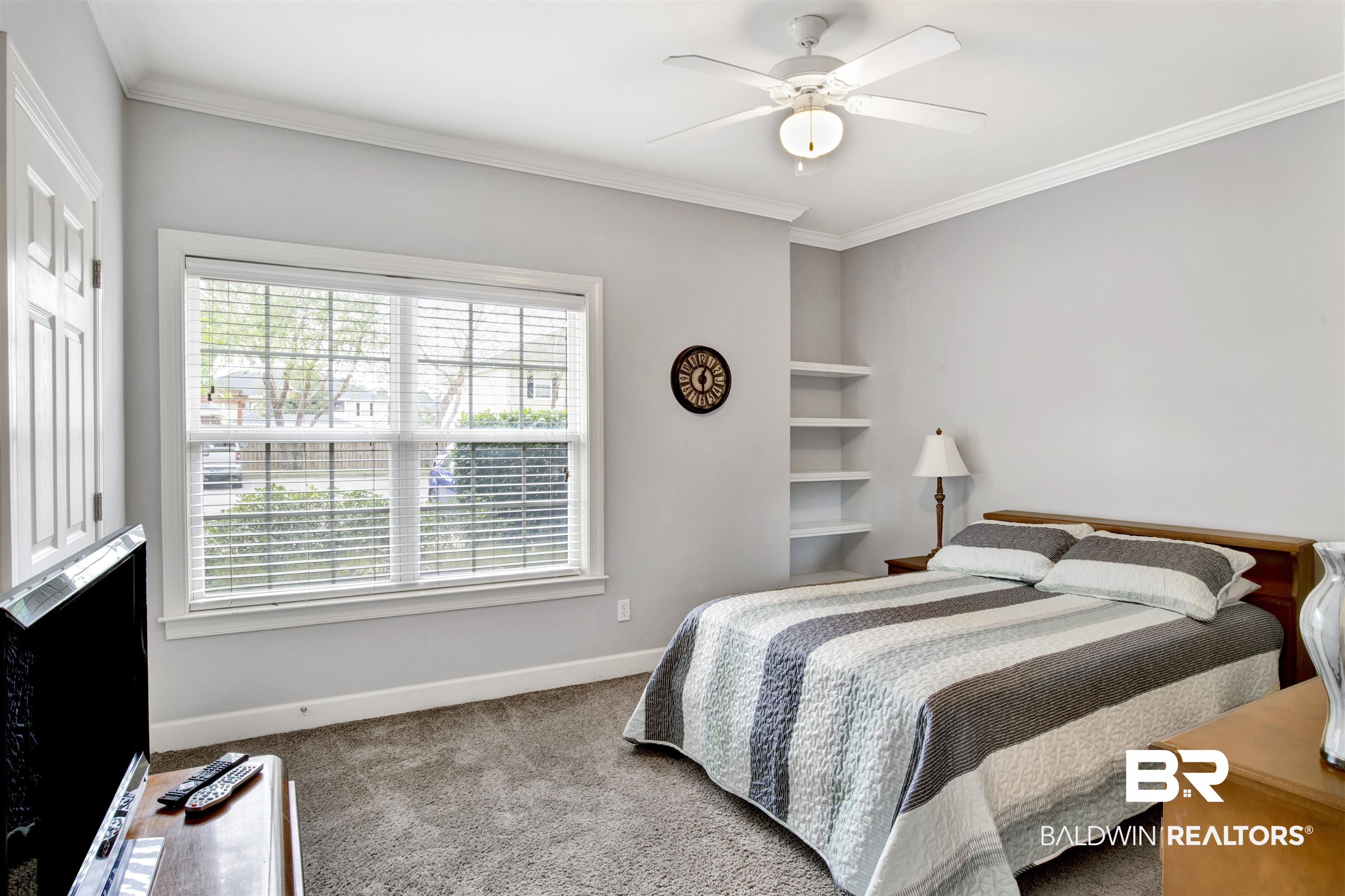 Bedroom with a striped quilt, large window with blinds, and built-in shelves.