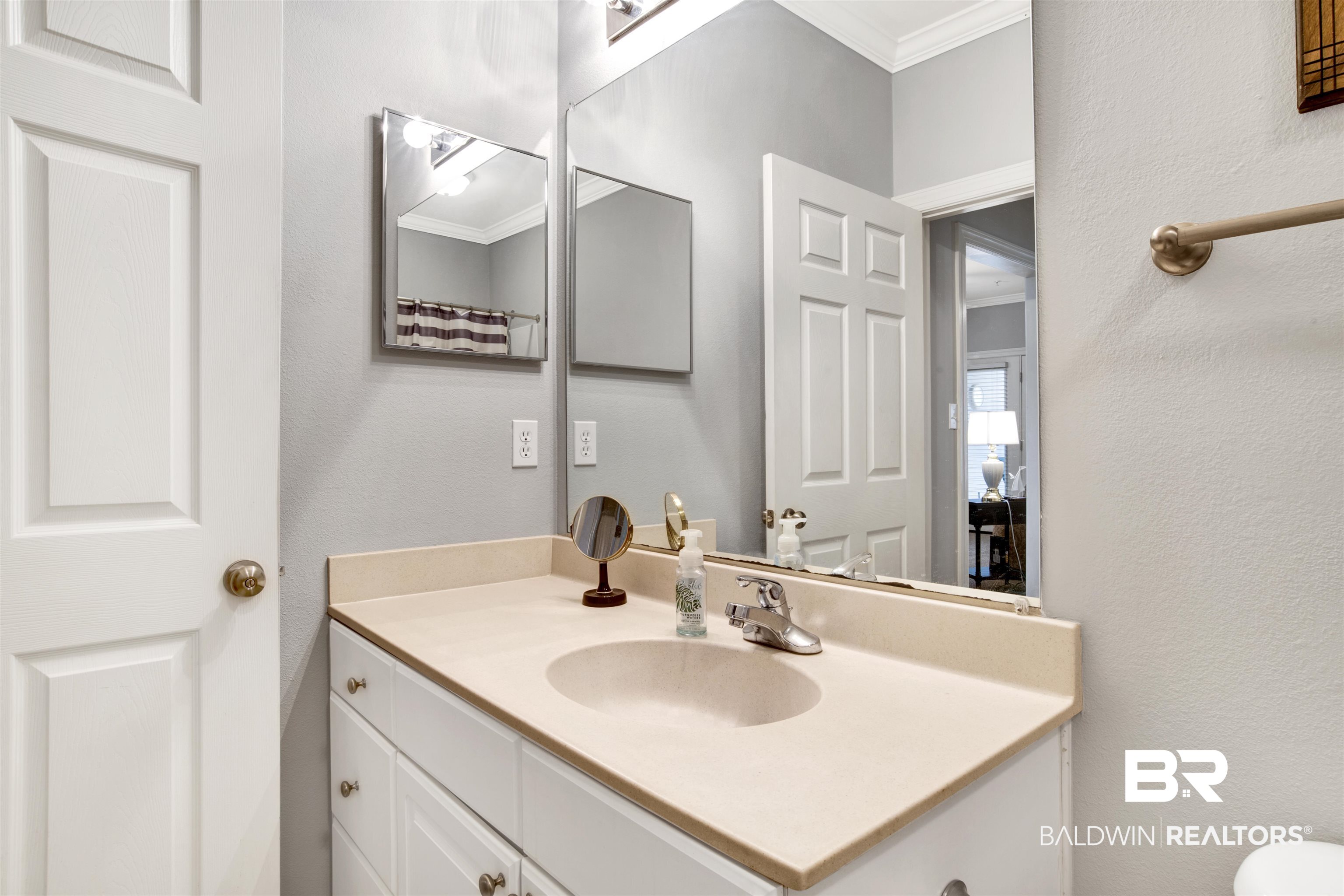 Bathroom vanity with a beige countertop, oval sink, large mirror, and white cabinetry.