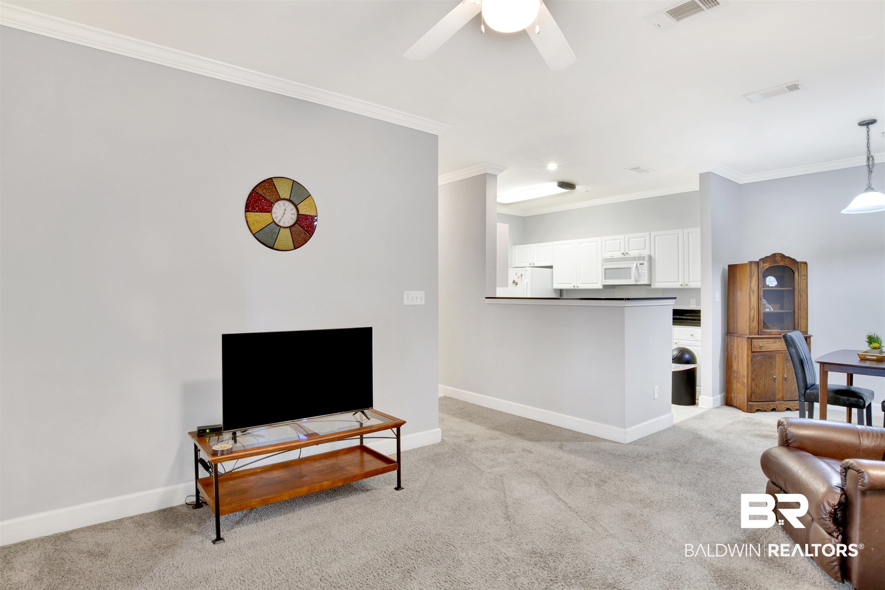 Open living room and kitchen with gray carpet, white cabinets, and leather seating.