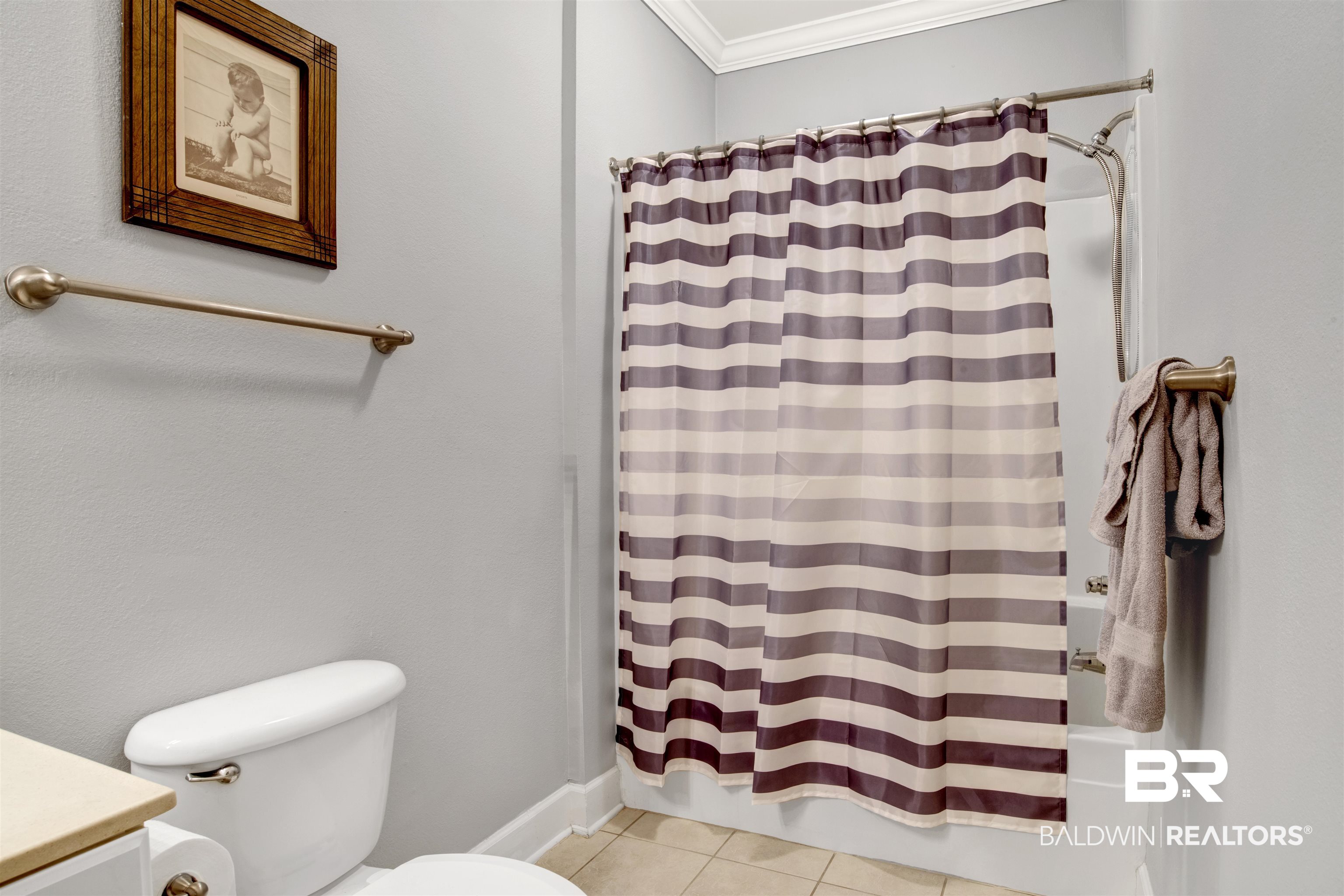 Bathroom with a mauve-and-cream striped shower curtain, brass fixtures, and framed wall art.