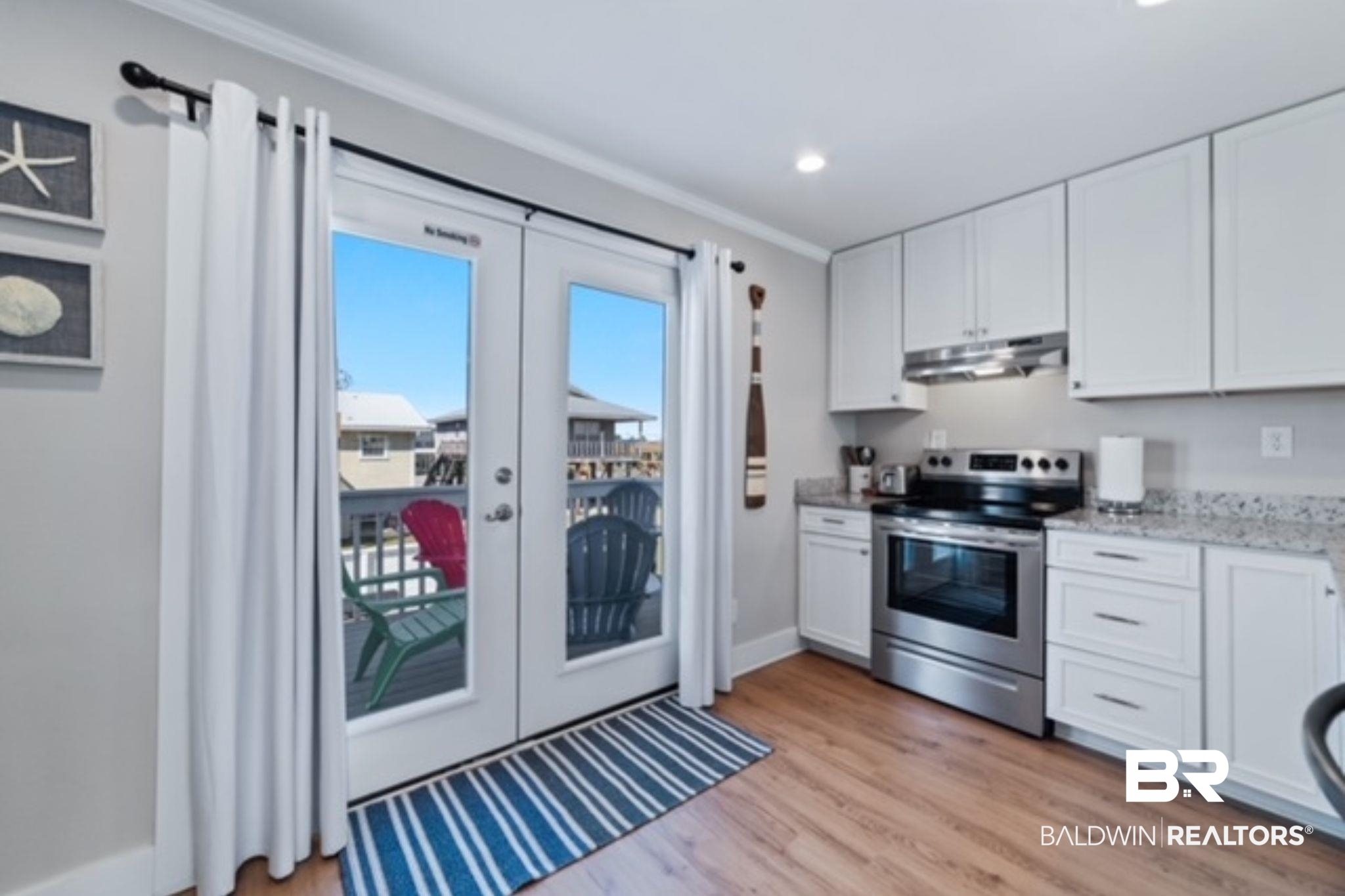 Kitchen with white cabinets and stainless steel range beside glass balcony doors and a blue striped rug.