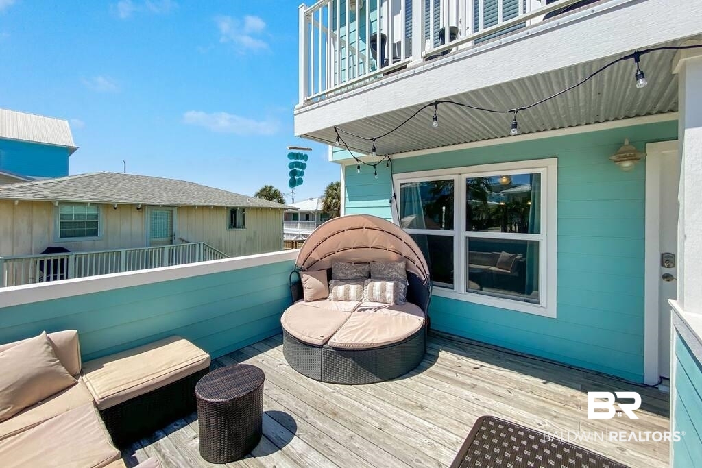 Furnished wooden deck with turquoise siding, a cushioned daybed, and string lights.