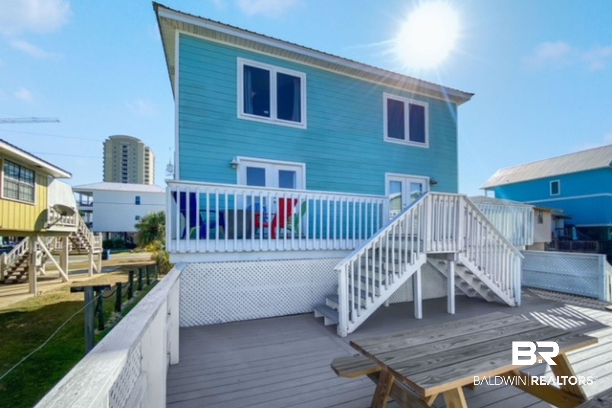 Turquoise coastal home with a raised white-railed deck, exterior stairs, and a picnic table.