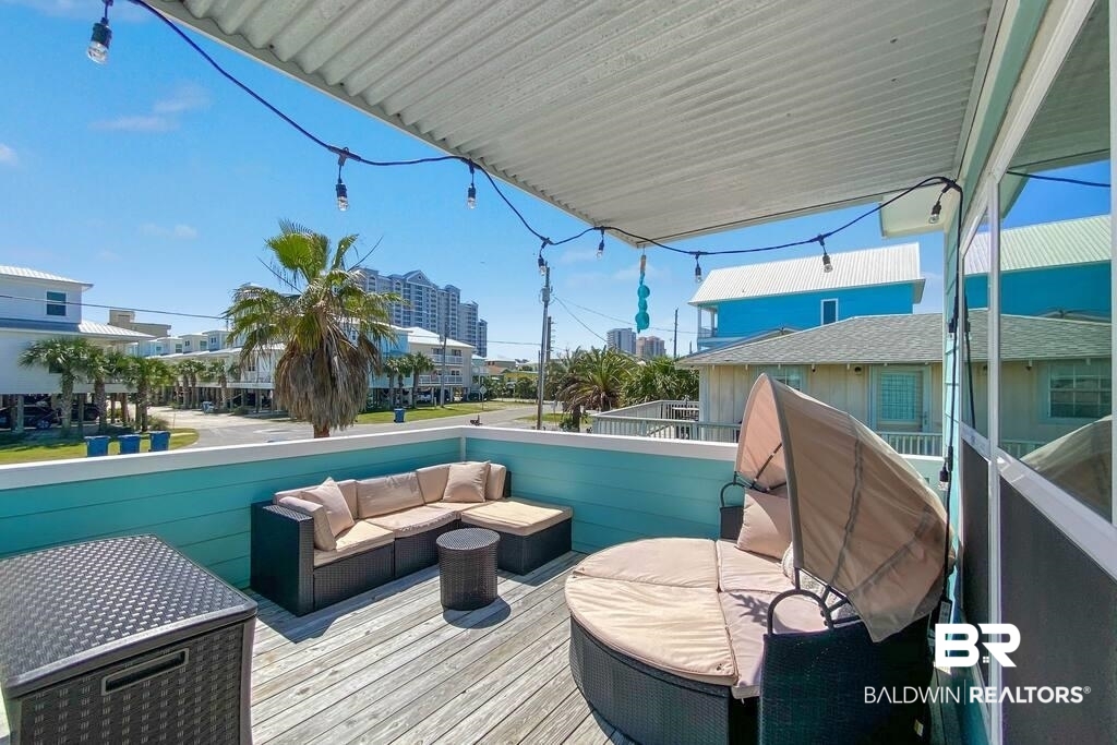 Furnished outdoor deck with turquoise railings, wicker seating, string lights, and palm trees nearby.