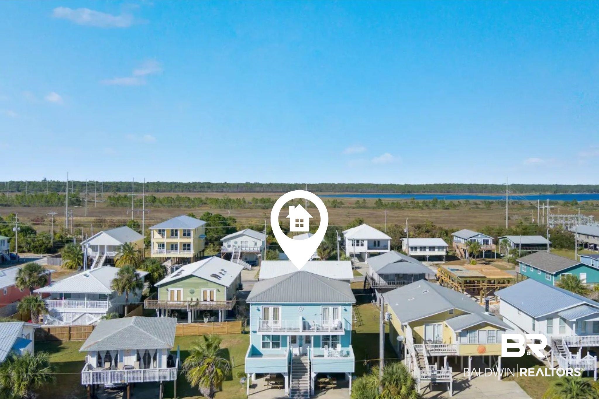 Aerial view of raised coastal homes, with a blue house marked in the foreground and water beyond.