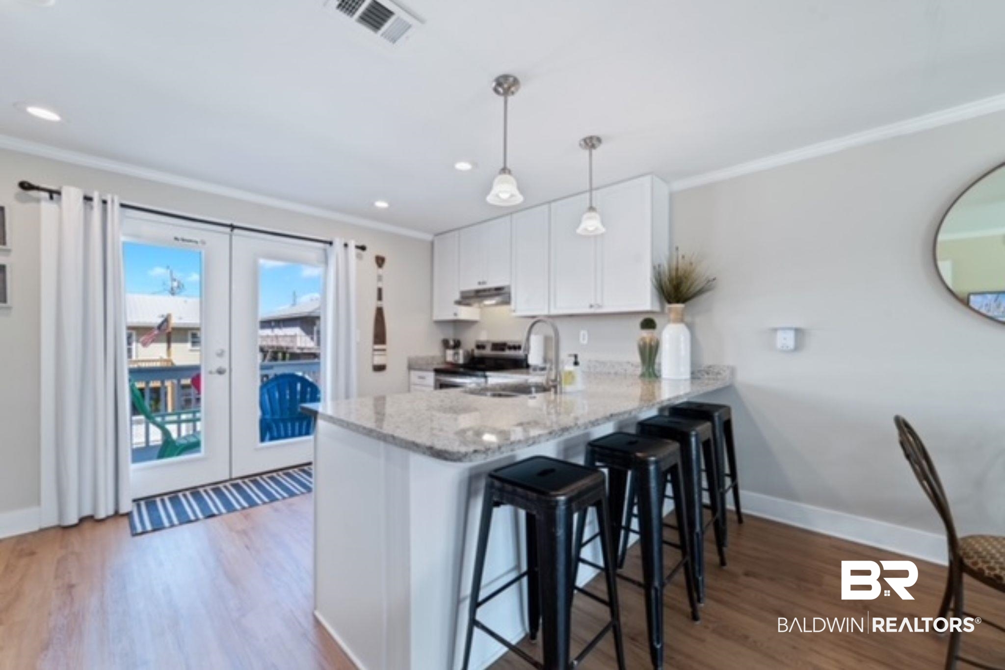 Kitchen with a granite island and black stools beside glass balcony doors.
