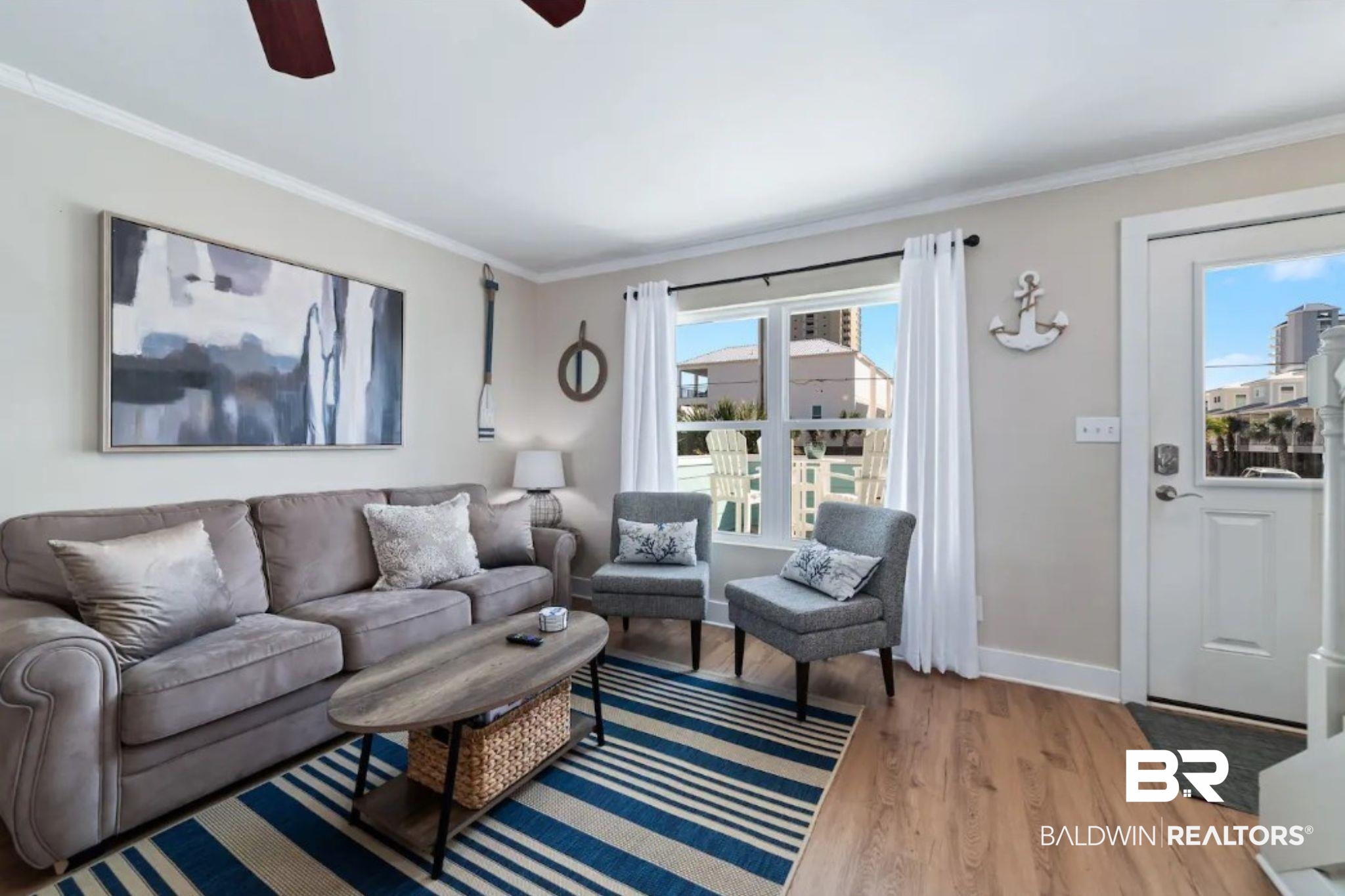 Furnished living room with gray seating, a striped blue rug, and coastal decor.