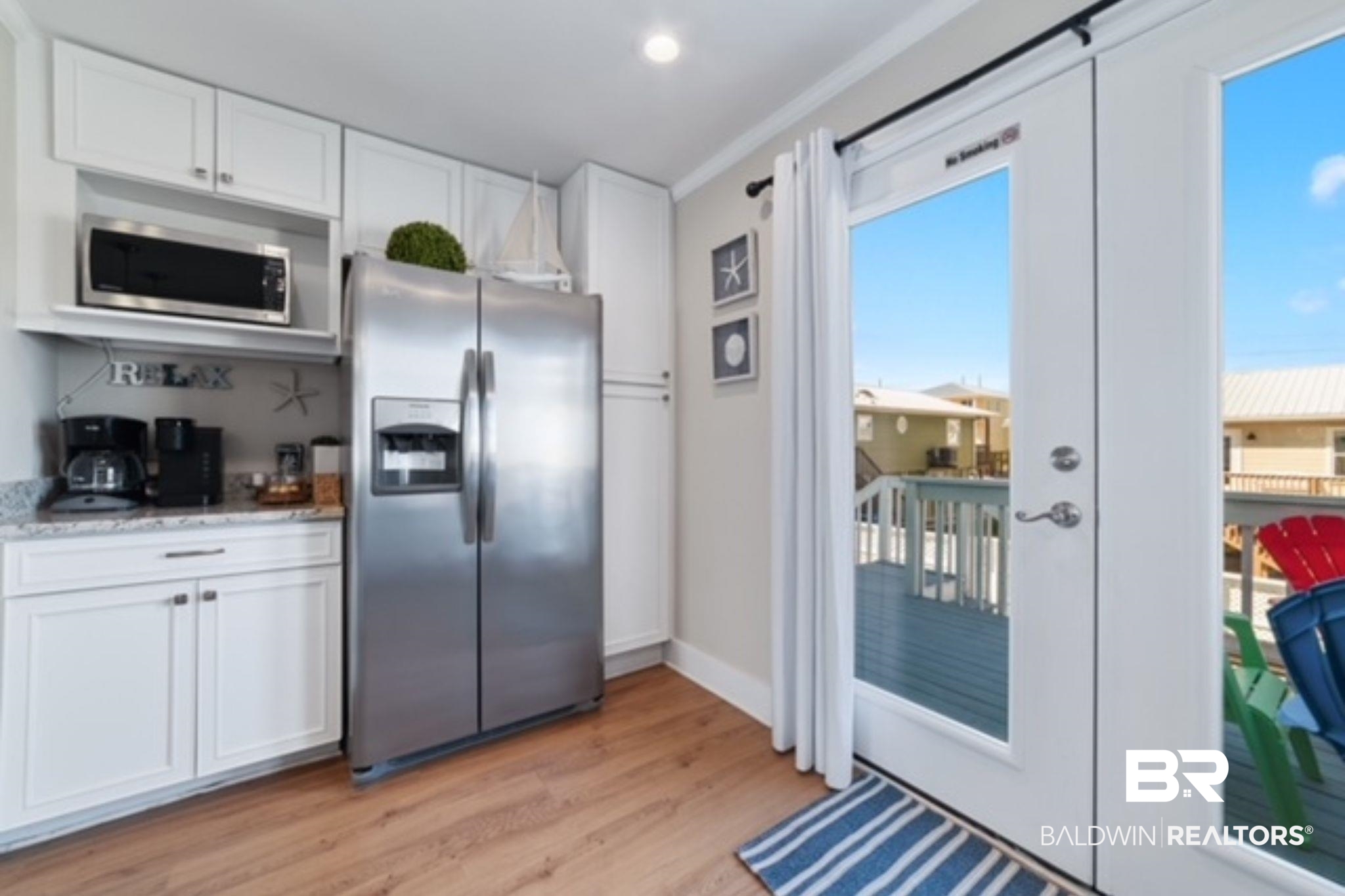Bright kitchen with white cabinets and stainless appliances beside an open door to a deck.