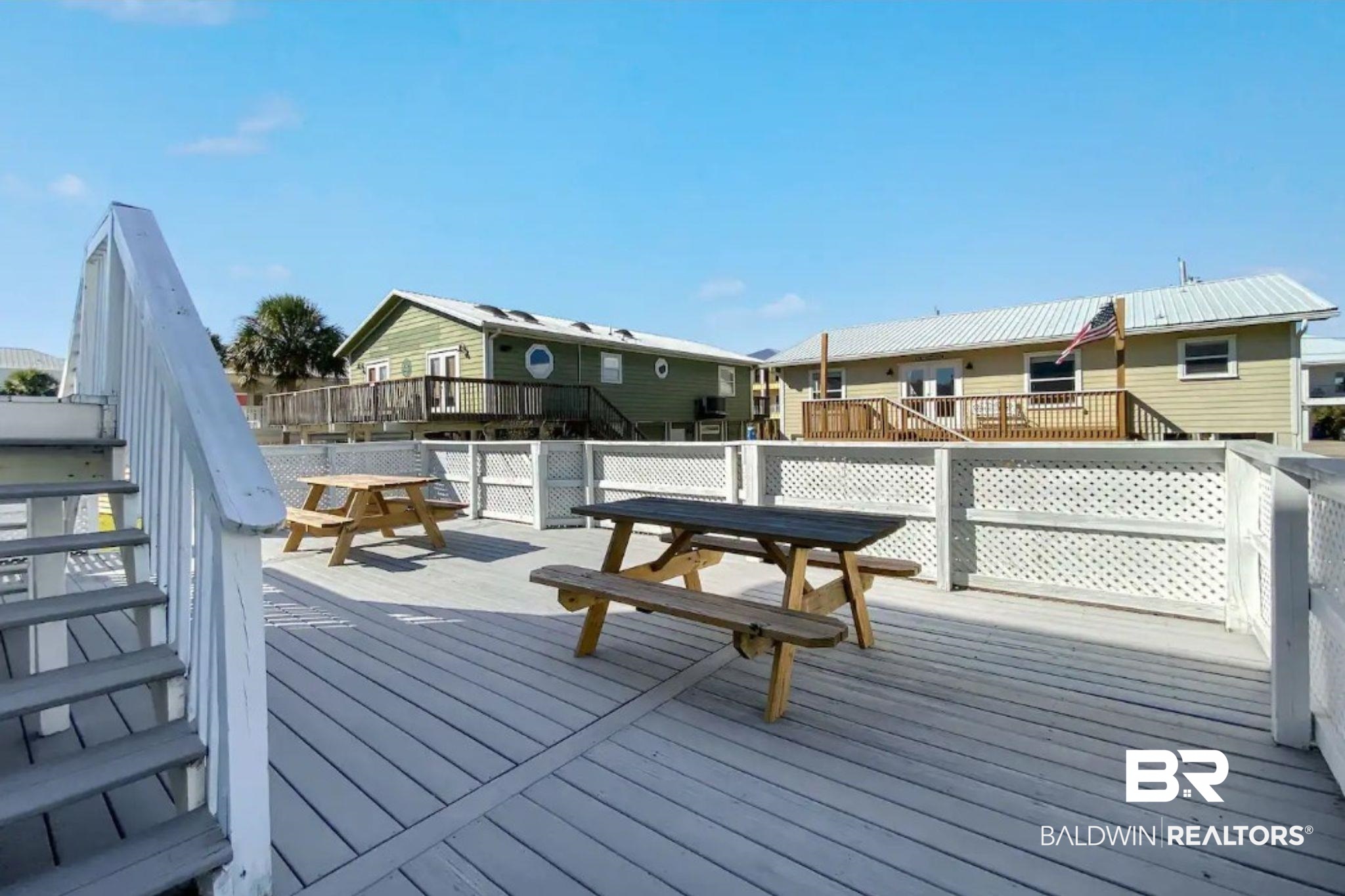 Outdoor deck with two picnic tables, white lattice railings, and stairs.
