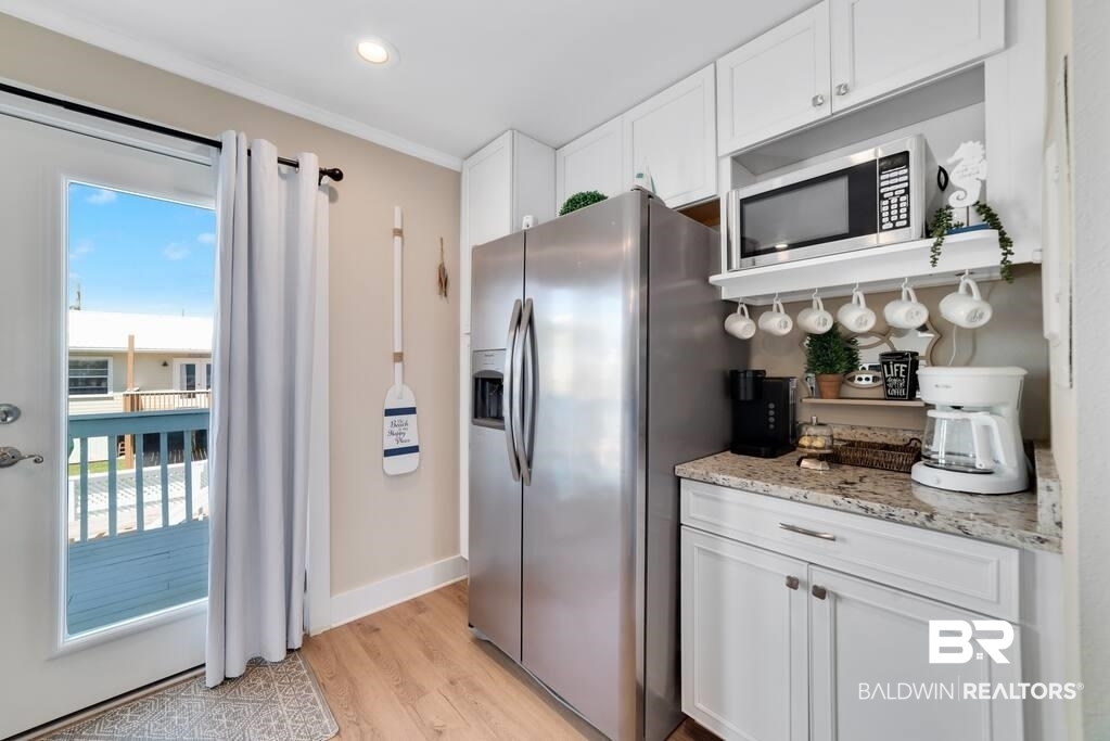 Kitchen with white cabinets and stainless steel appliances beside a glass door to a blue-railed deck.