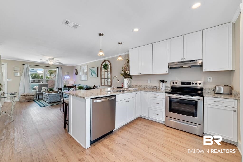 Open-plan kitchen with white cabinetry, stainless steel appliances, and a granite island beside the living area.