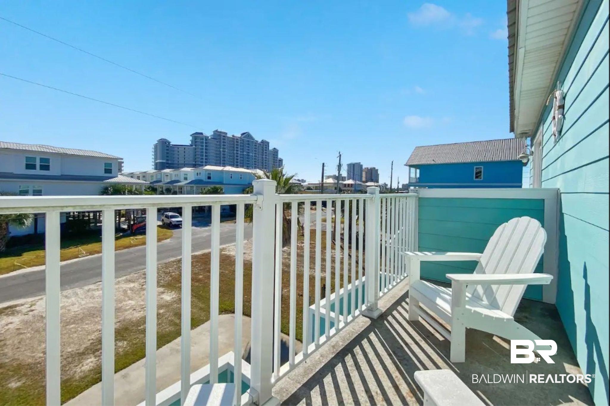 Balcony with a white Adirondack chair, white railing, and views of nearby buildings.