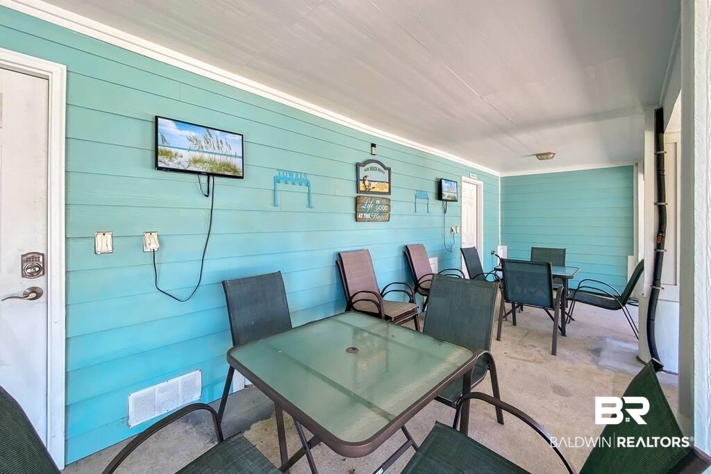 Covered patio with turquoise siding, glass-top tables, woven chairs, and wall-mounted televisions.
